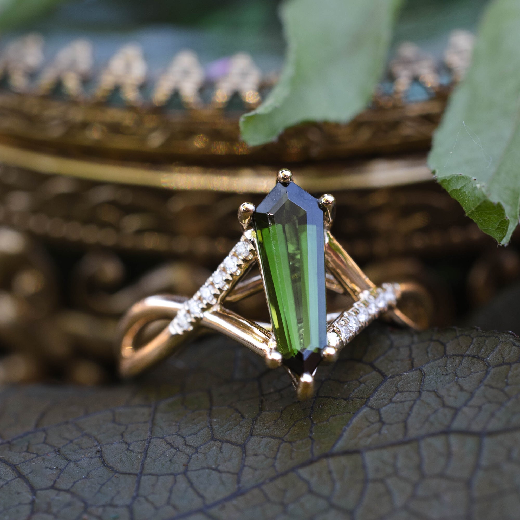 Gold ring with a green tourmaline and diamond accents on a leafy background