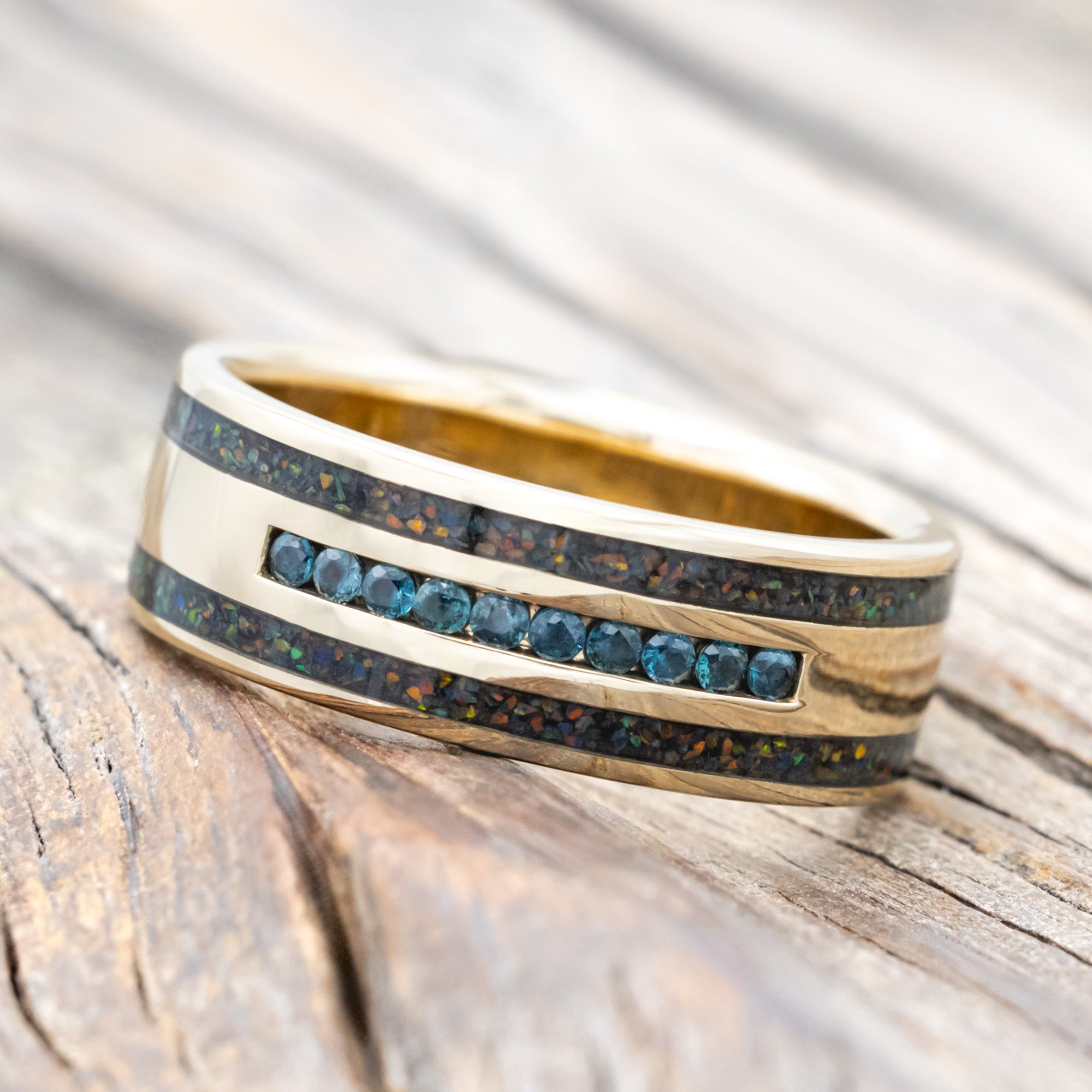 Yellow gold ring with alexandrite accents and black fire opal inlays on a wooden surface