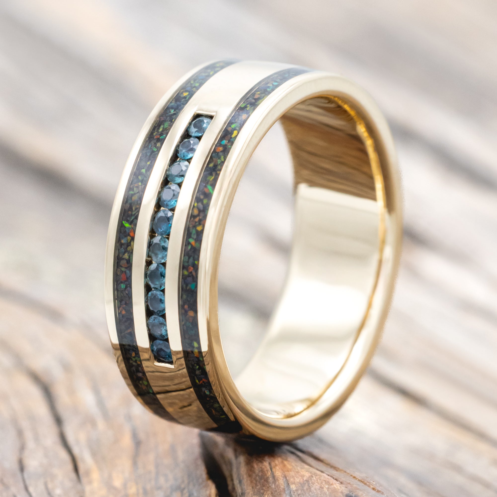 Yellow gold ring with alexandrite accents and black fire opal inlays on a wooden surface