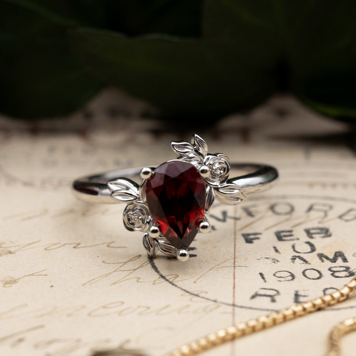 White ring with a garnet gemstone on an old document with a gold chain.