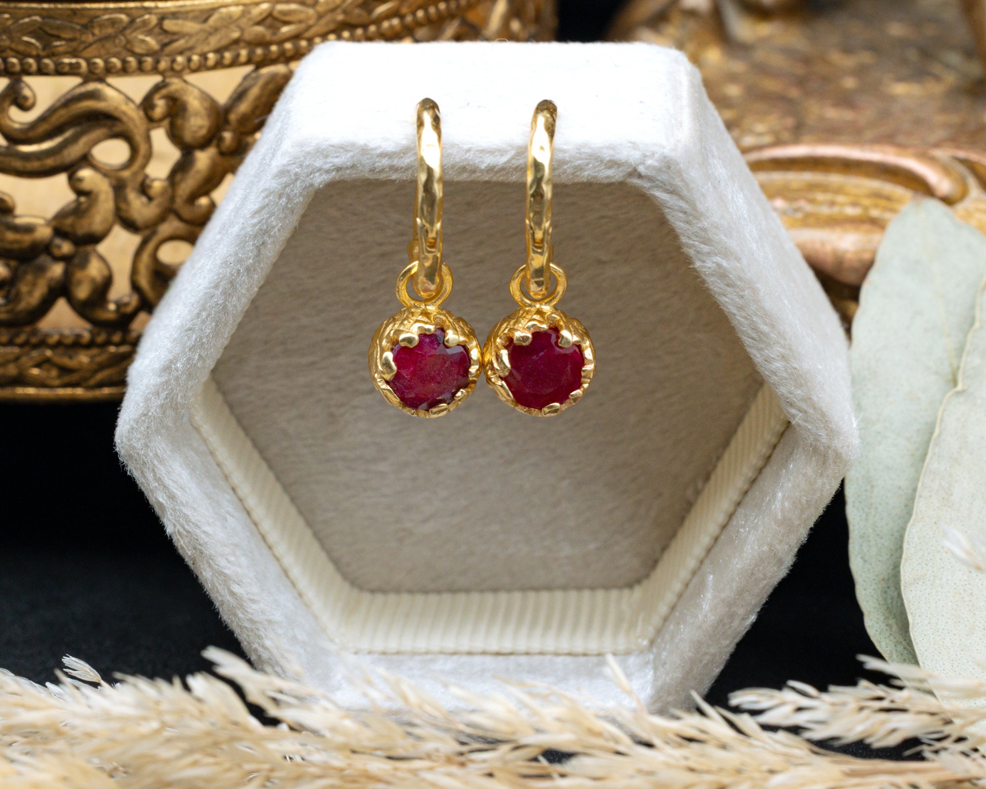 Gold earrings with red rubies in a hexagonal display box.