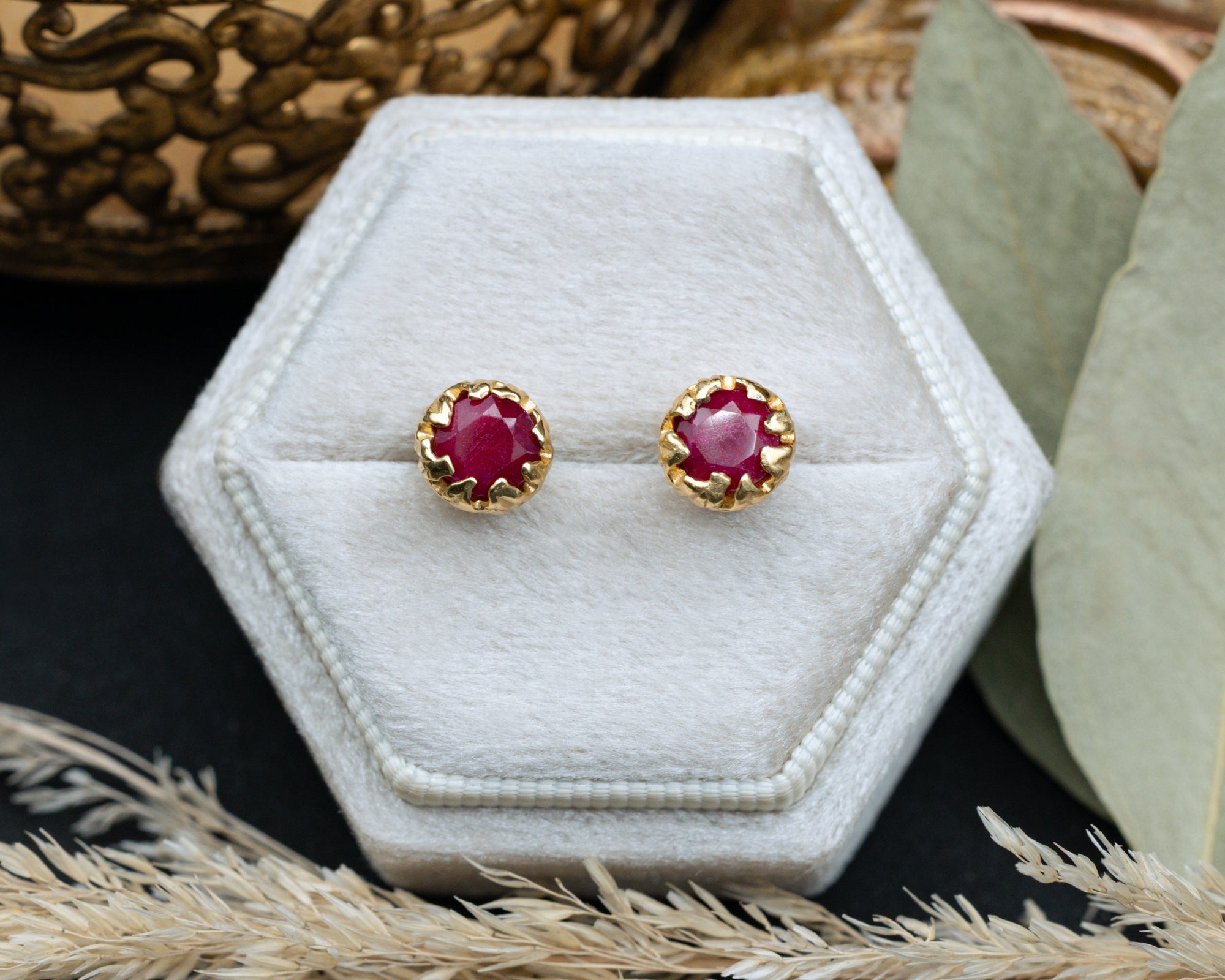Pair of ruby stud earrings in a hexagonal white jewelry box.