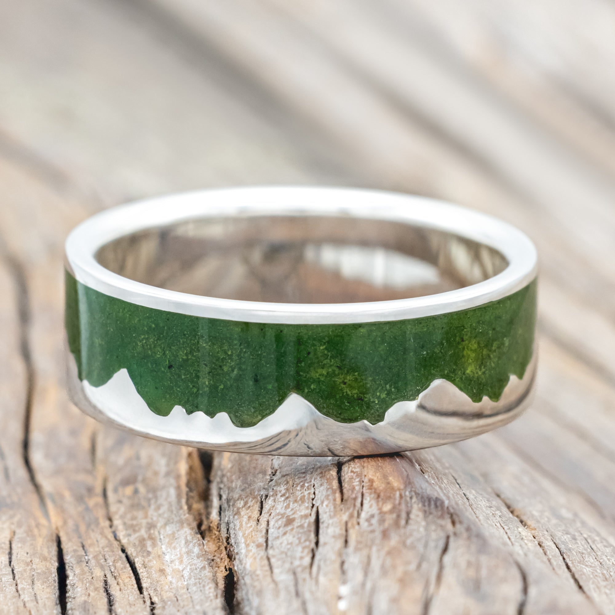 Silver ring with moss inlay and mountain range design on a wooden surface