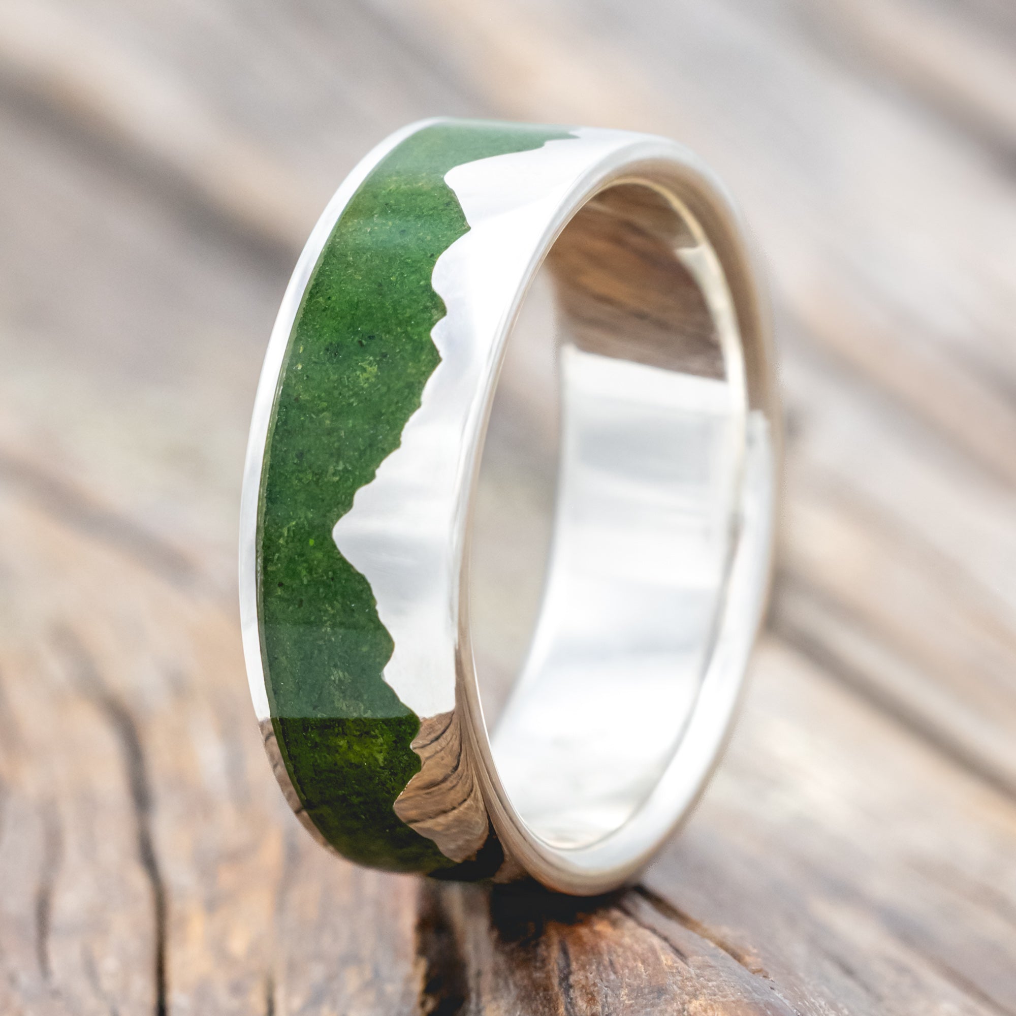 Silver ring with moss inlay and mountain range design on a wooden surface