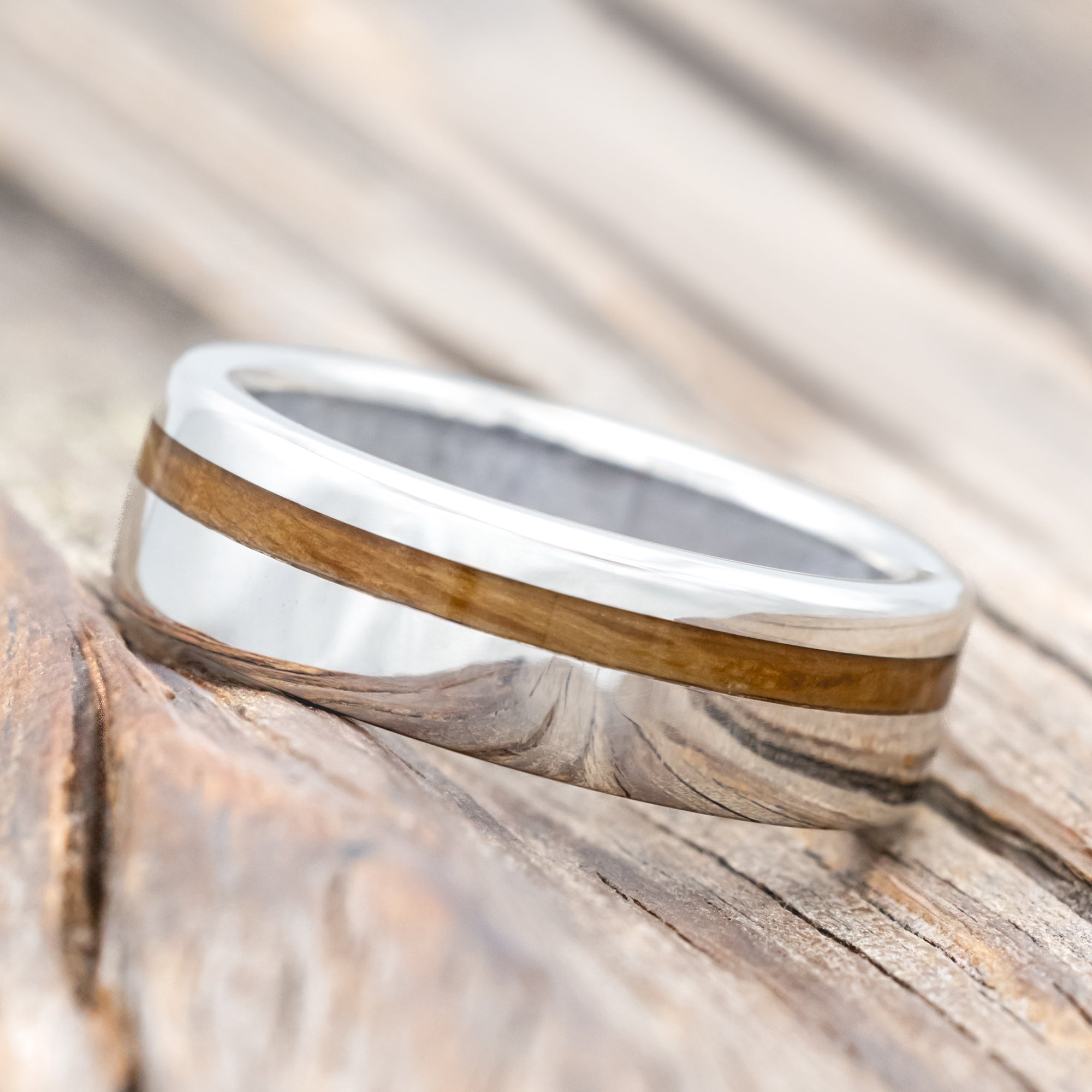 Silver ring with whiskey barrel inlay and wedding dress lining on a wooden surface