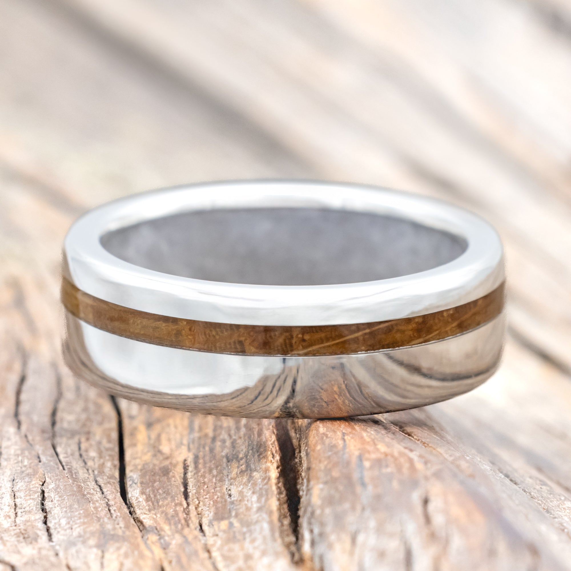 Silver ring with whiskey barrel inlay and wedding dress lining on a wooden surface