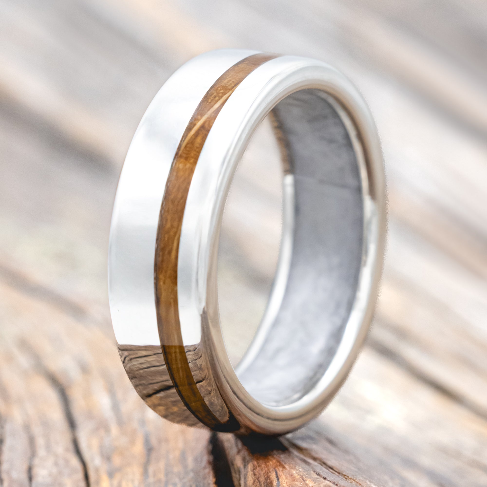 Silver ring with whiskey barrel inlay and wedding dress lining on a wooden surface