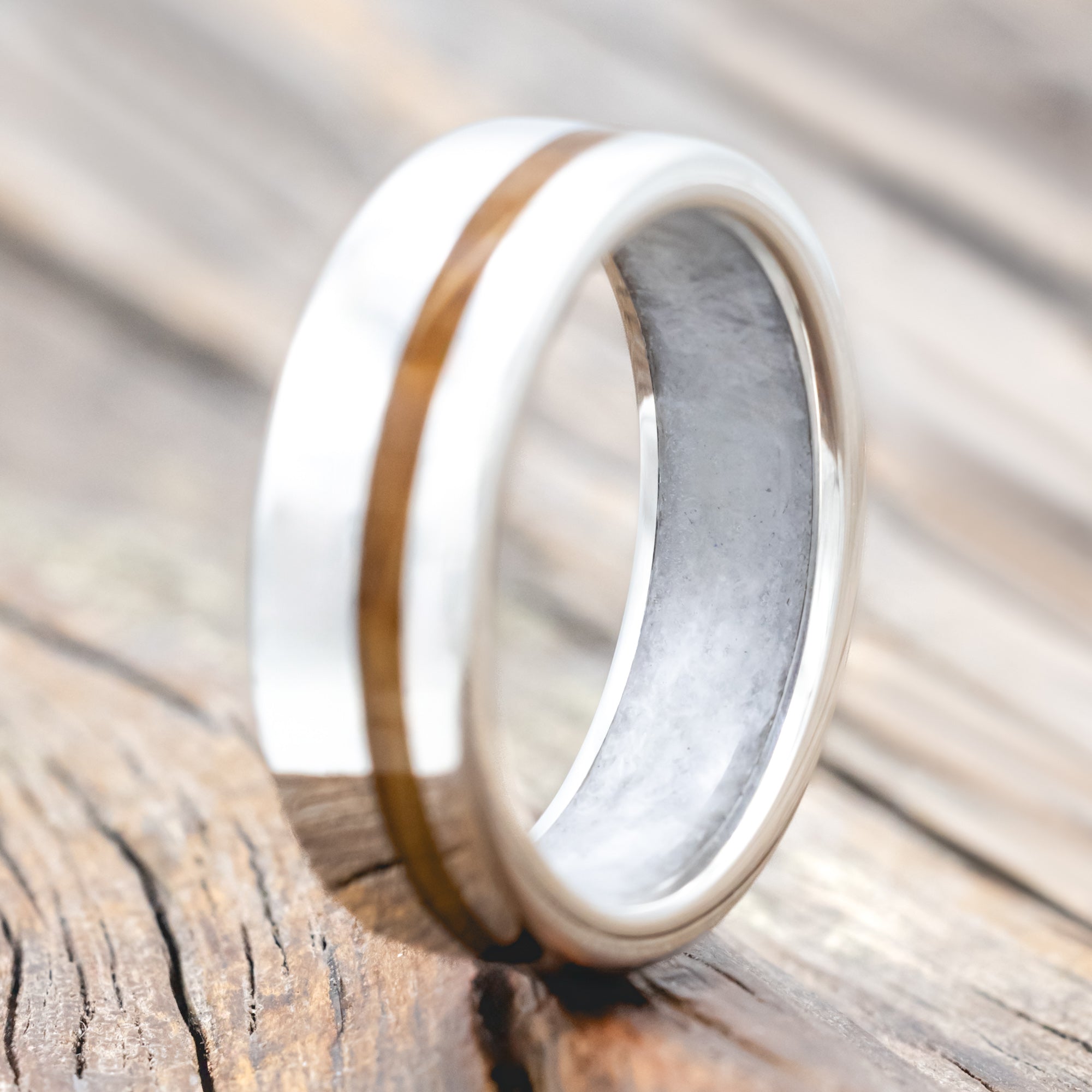Silver ring with whiskey barrel inlay and wedding dress lining on a wooden surface