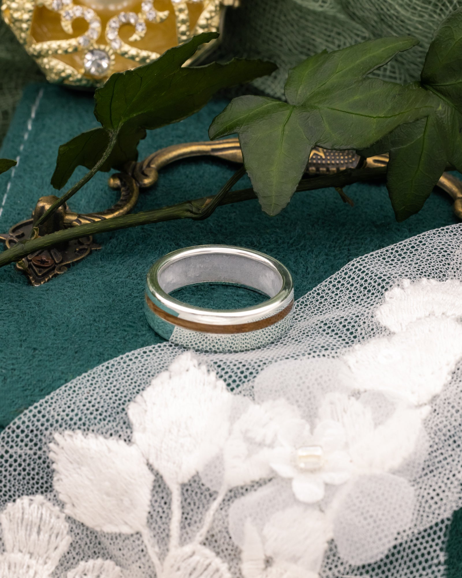 Silver ring with whiskey barrel inlay on a decorative surface with leaves and lace