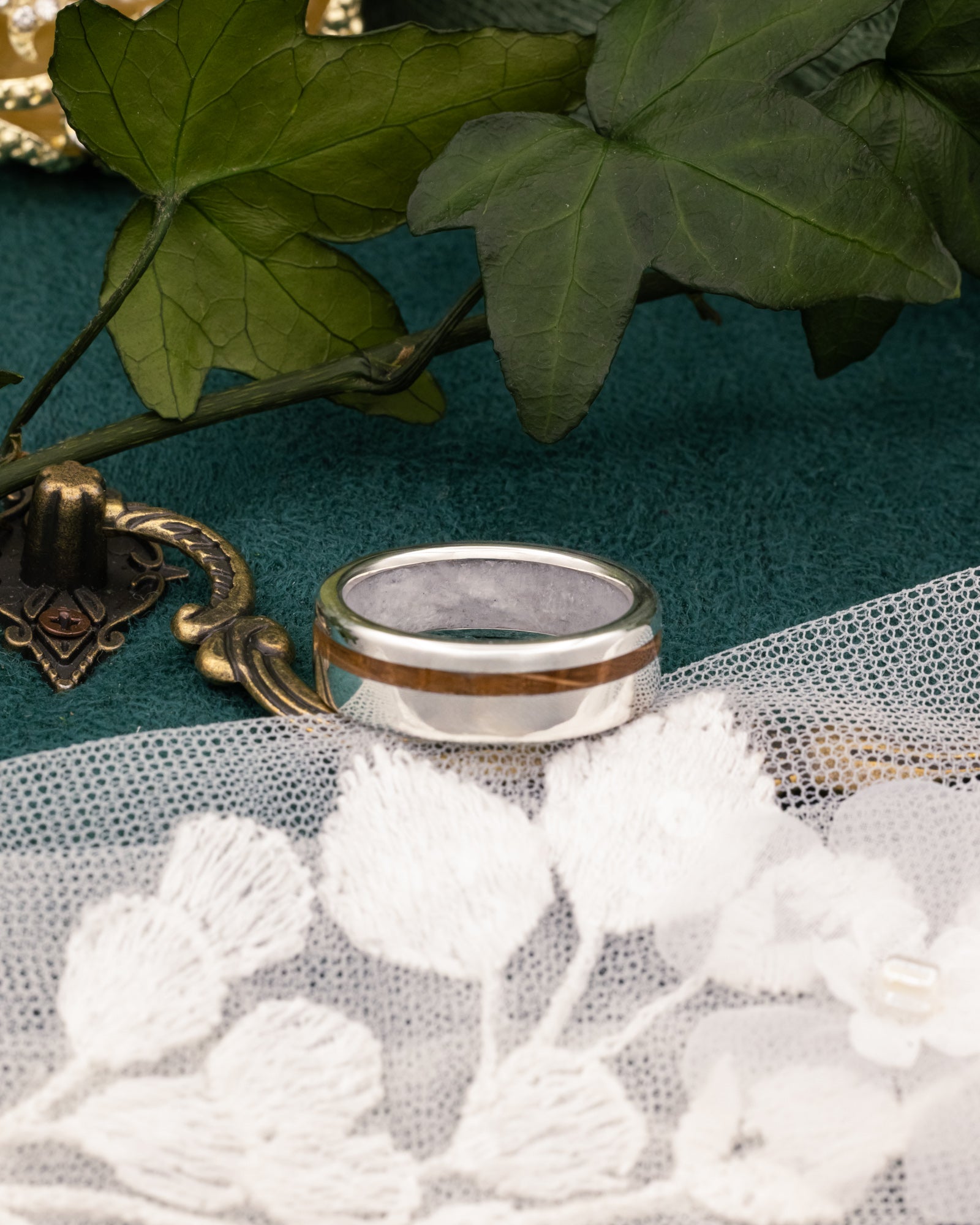 Silver ring with whiskey barrel inlay on a decorative surface with leaves and lace