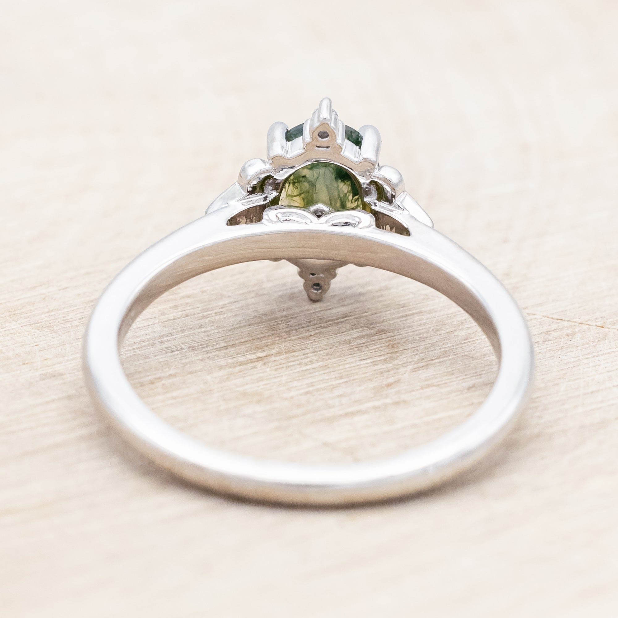14K white gold engagement ring with moss agate and diamond accents on a light wooden surface