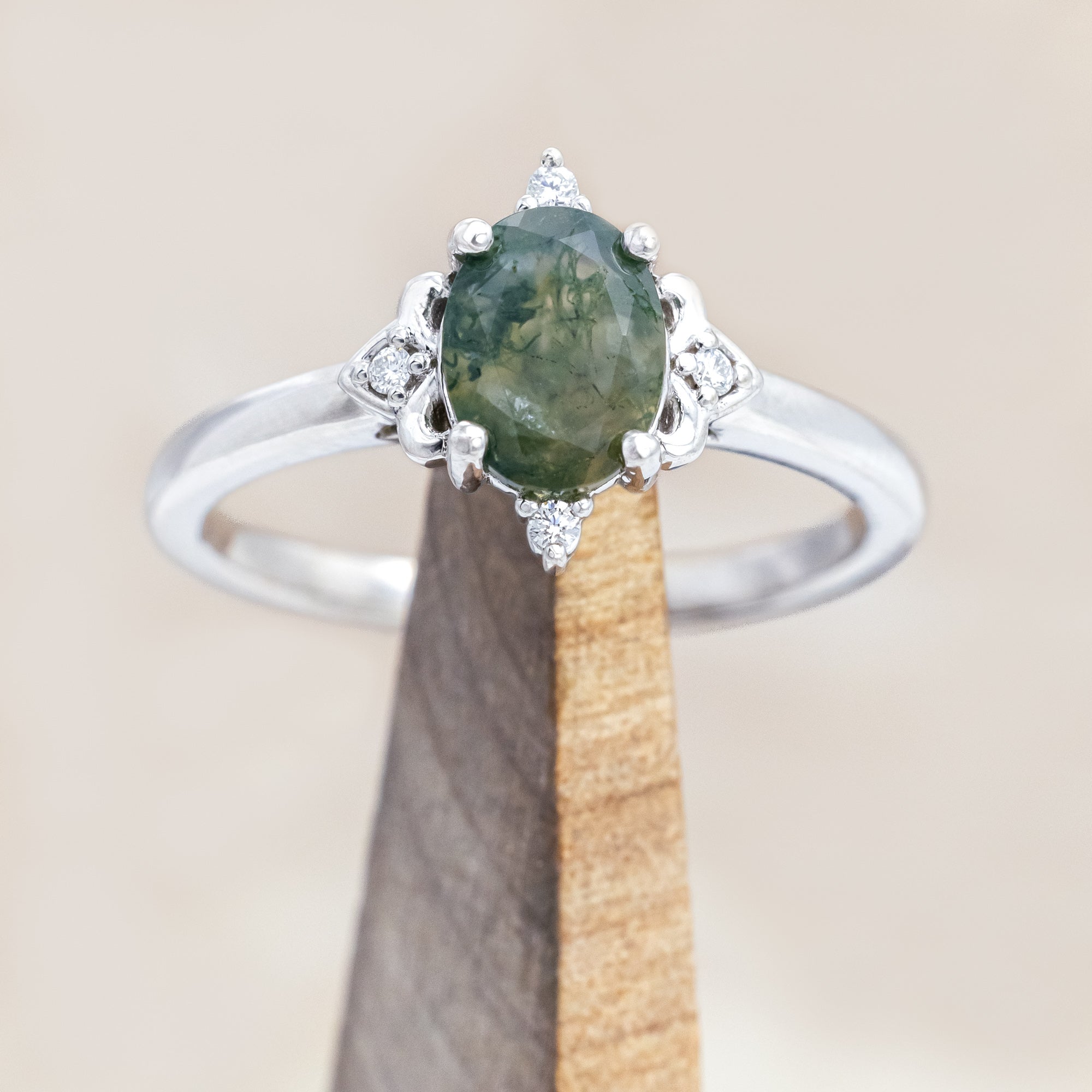 14K white gold engagement ring with moss agate and diamond accents on a light wooden surface