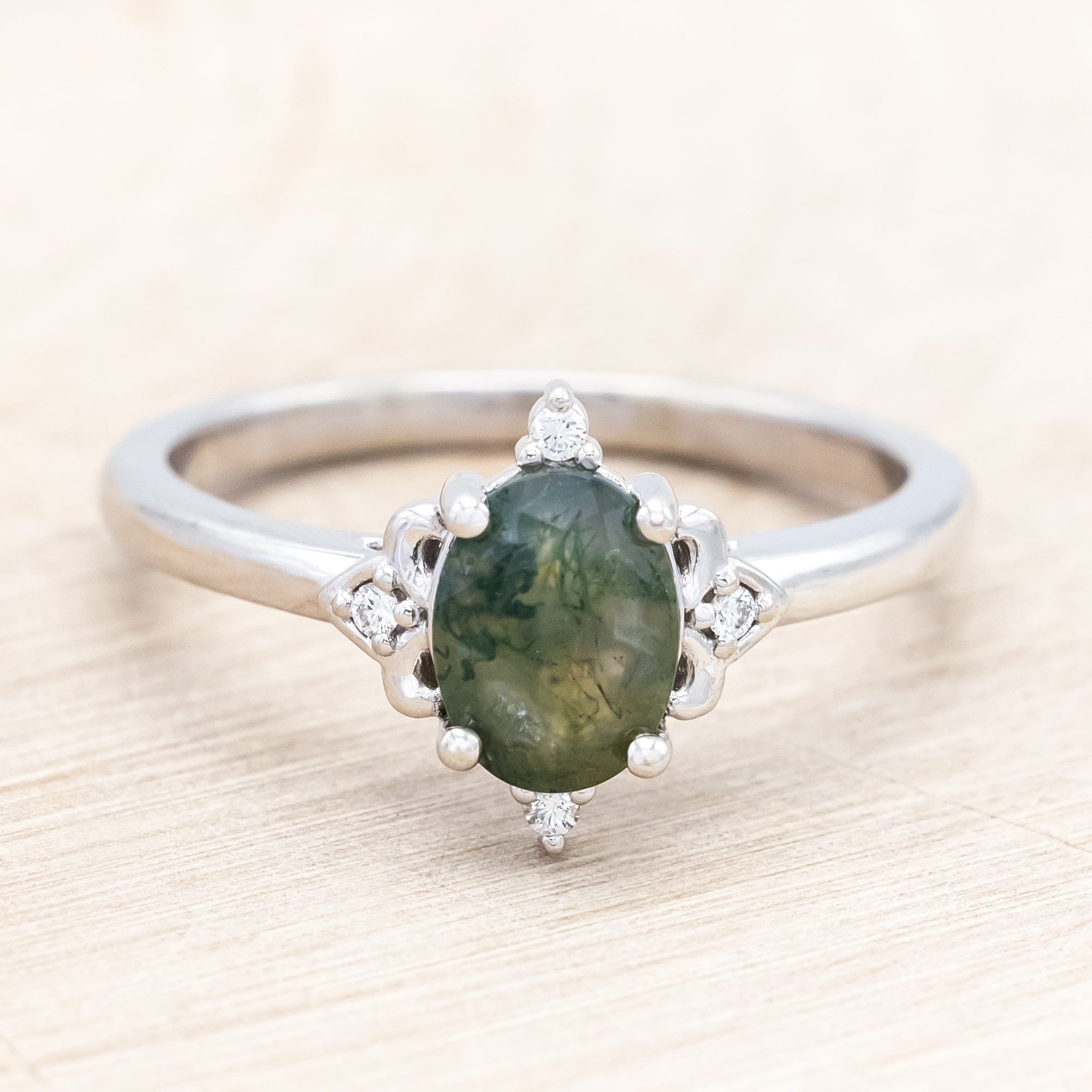 14K white gold engagement ring with moss agate and diamond accents on a light wooden surface