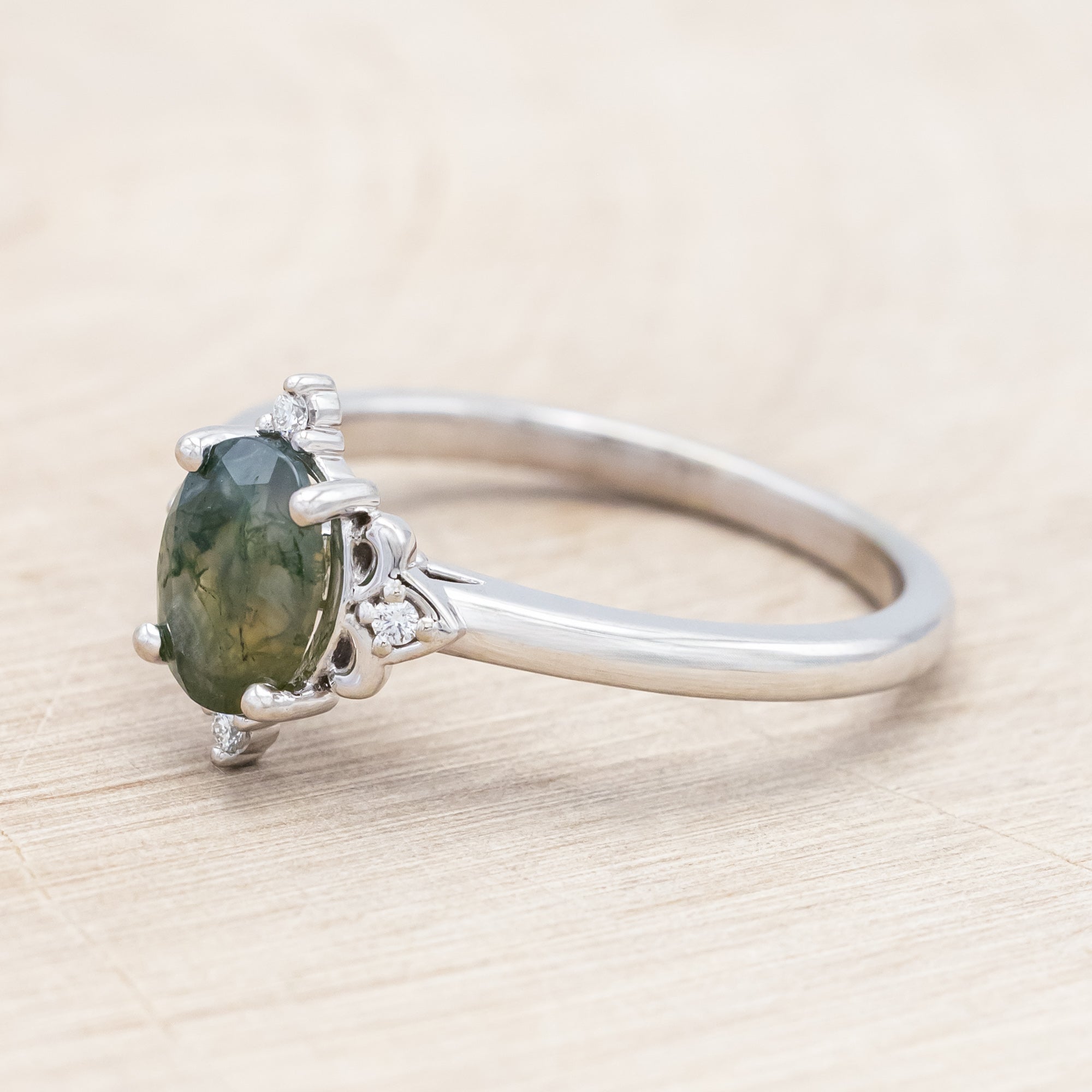 14K white gold engagement ring with moss agate and diamond accents on a light wooden surface