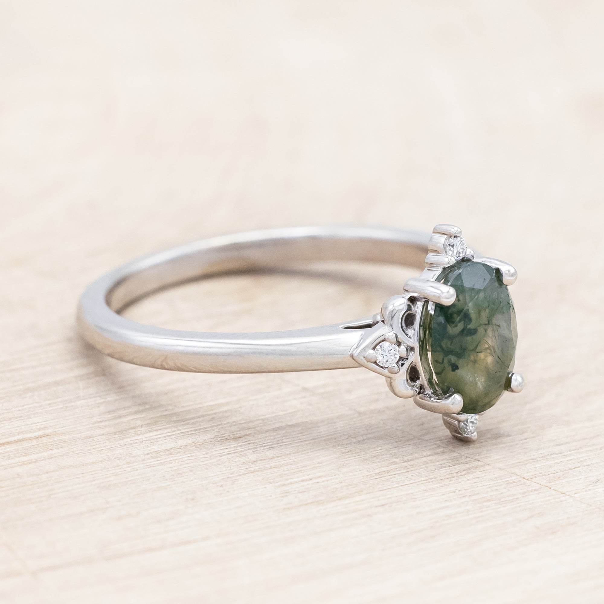 14K white gold engagement ring with moss agate and diamond accents on a light wooden surface