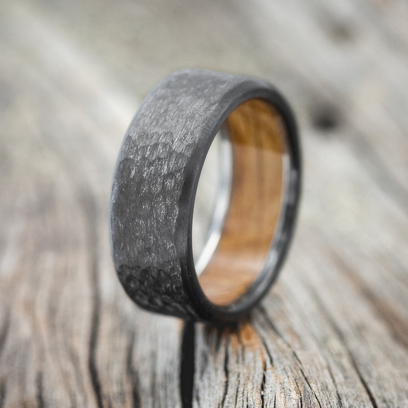 Shown here is a handcrafted men's wedding ring featuring a whiskey barrel oak lining and a hammered finish, upright facing left.