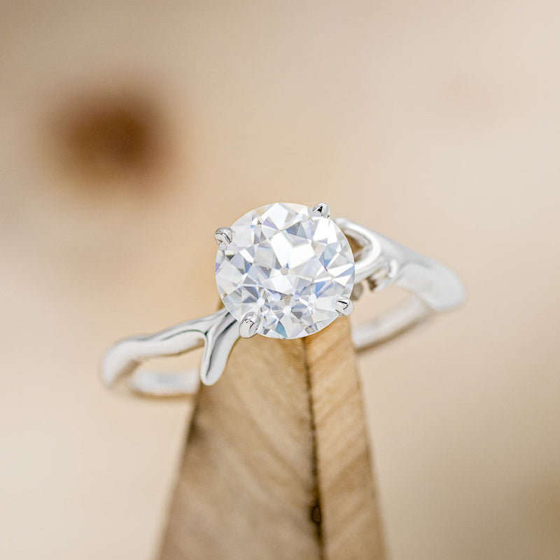 Shown here is "Artemis", a moissanite women's engagement ring with an antler/branch style band, on stand front facing. Many other center stone options are available upon request.