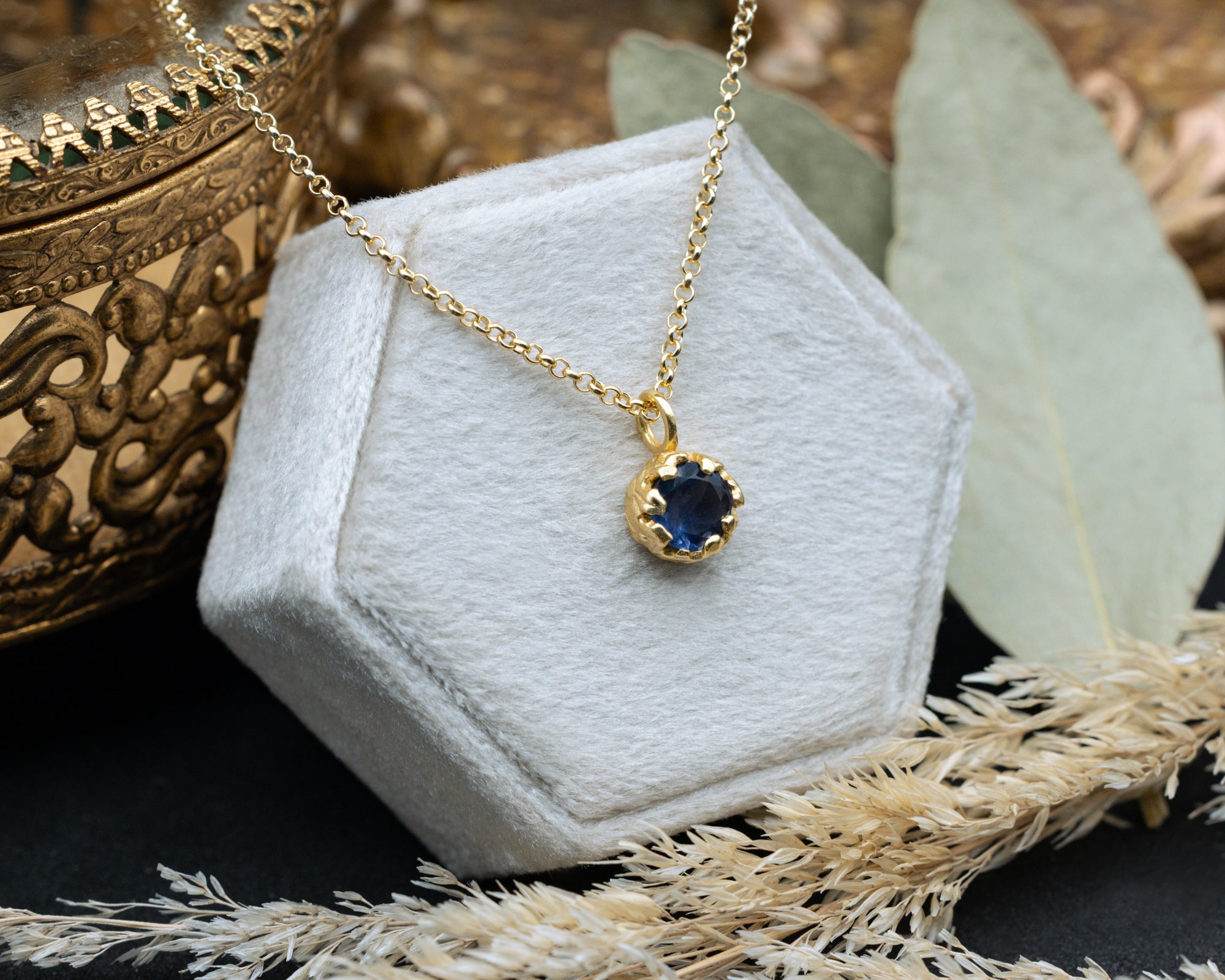 Gold necklace with a blue sapphire on a white hexagonal stand with decorative elements.