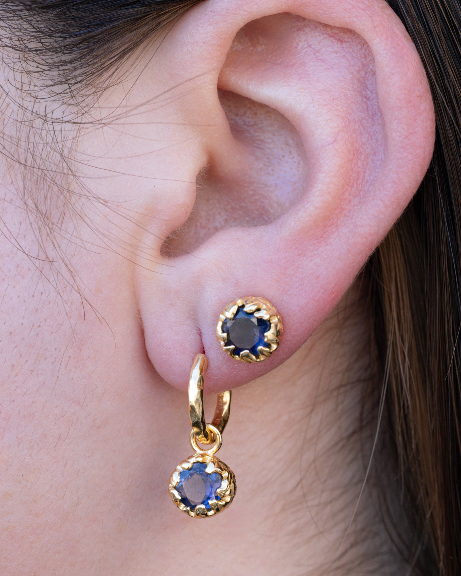 Close-up of an ear wearing gold hoop earrings with blue sapphires.