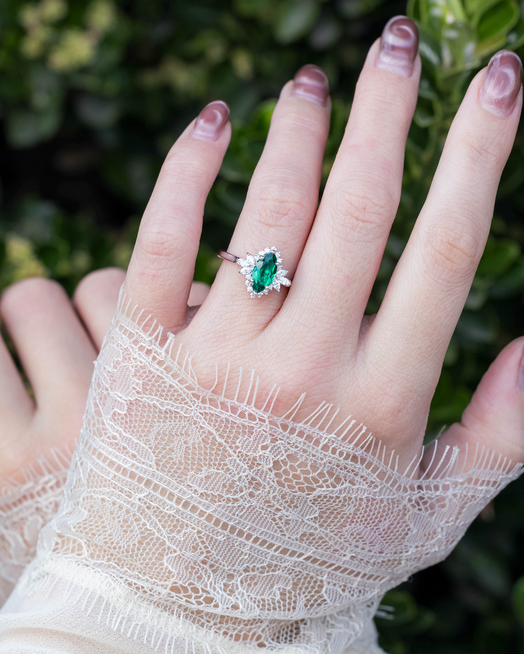 Hand wearing a lace glove with an emerald ring on a blurred green background