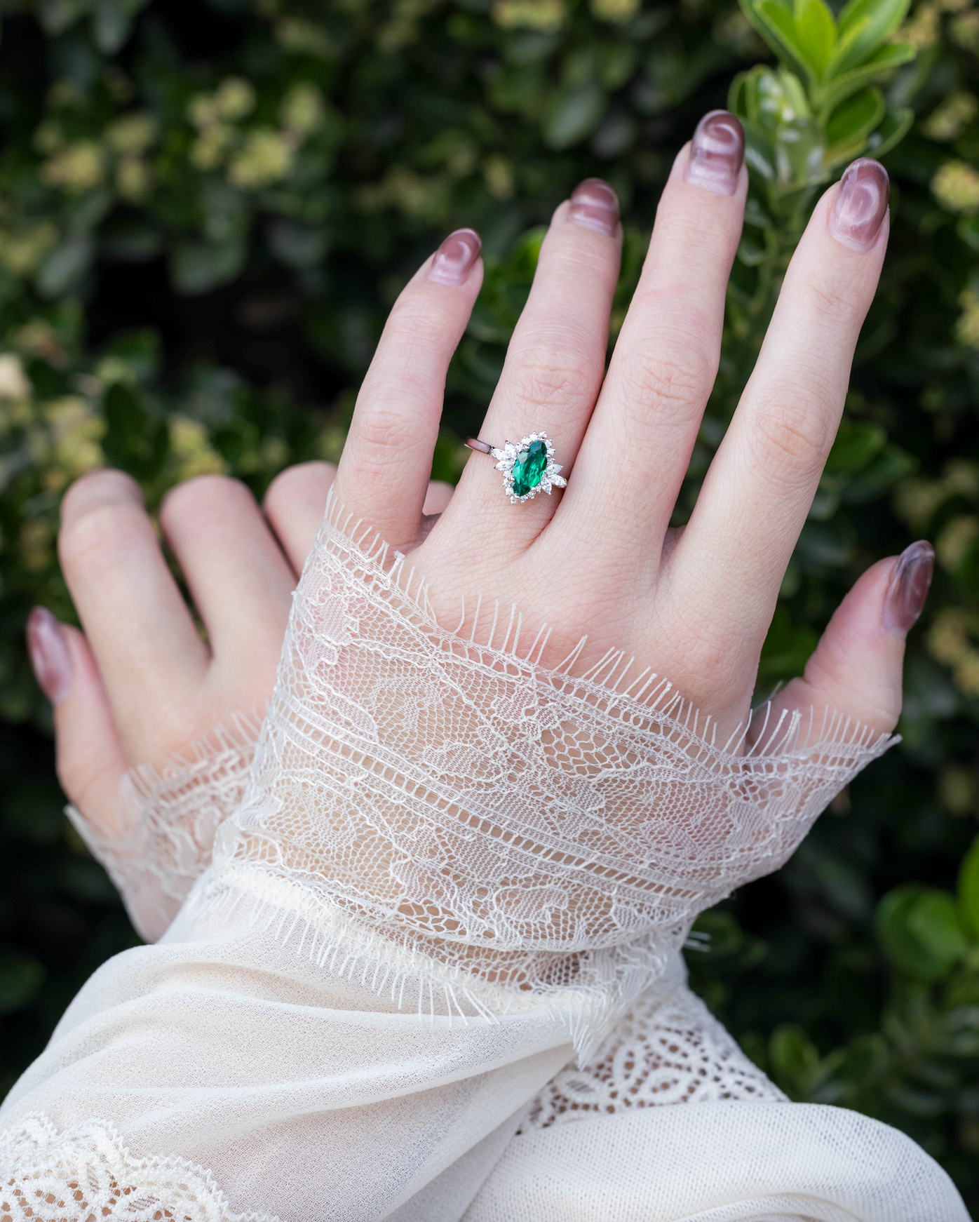 Hand wearing a lace glove with an emerald ring on a blurred green background