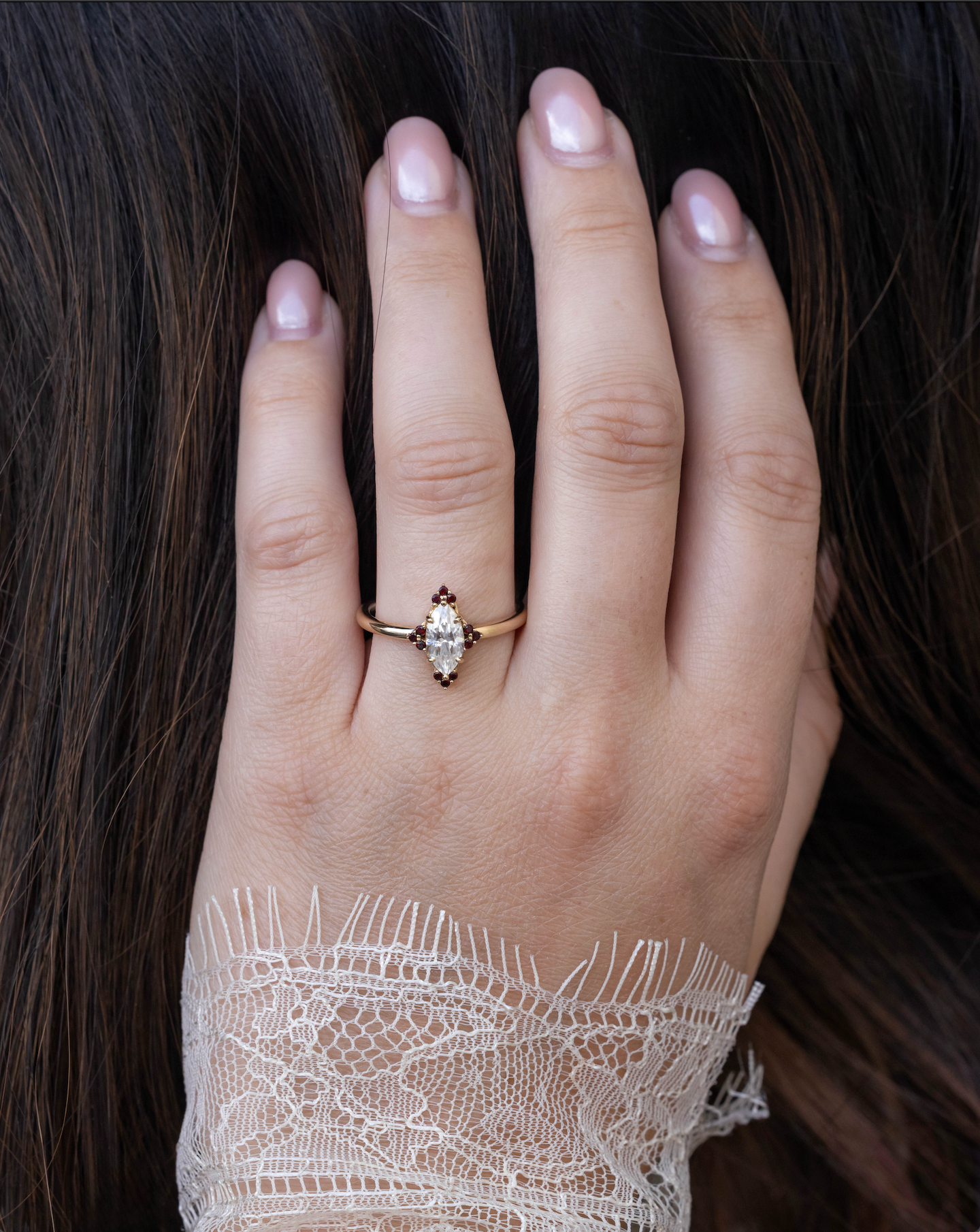Hand wearing a gold ring with a diamond center stone and small garnet accents on a dark background