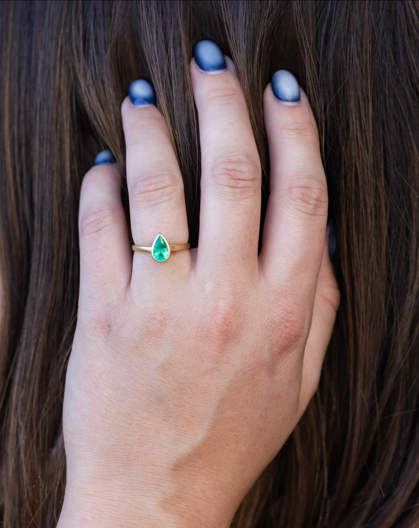 Hand wearing gold ring with emerald against dark hair