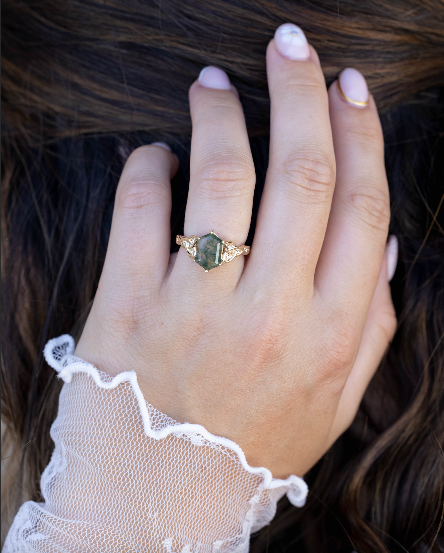 Hand wearing a gold ring with moss agate, wearing a lace glove.