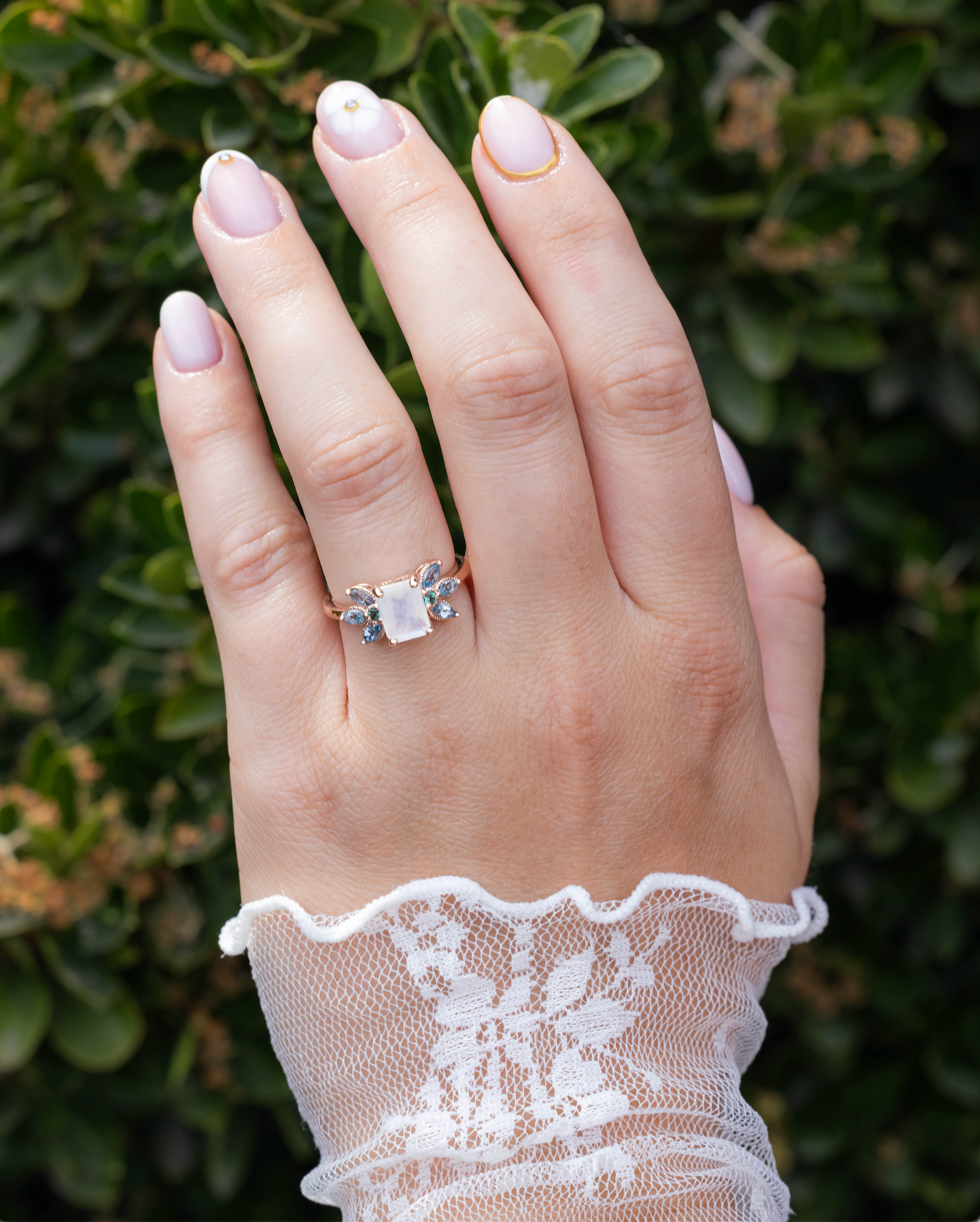 Hand wearing a ring with a moonstone, set against a blurred green background