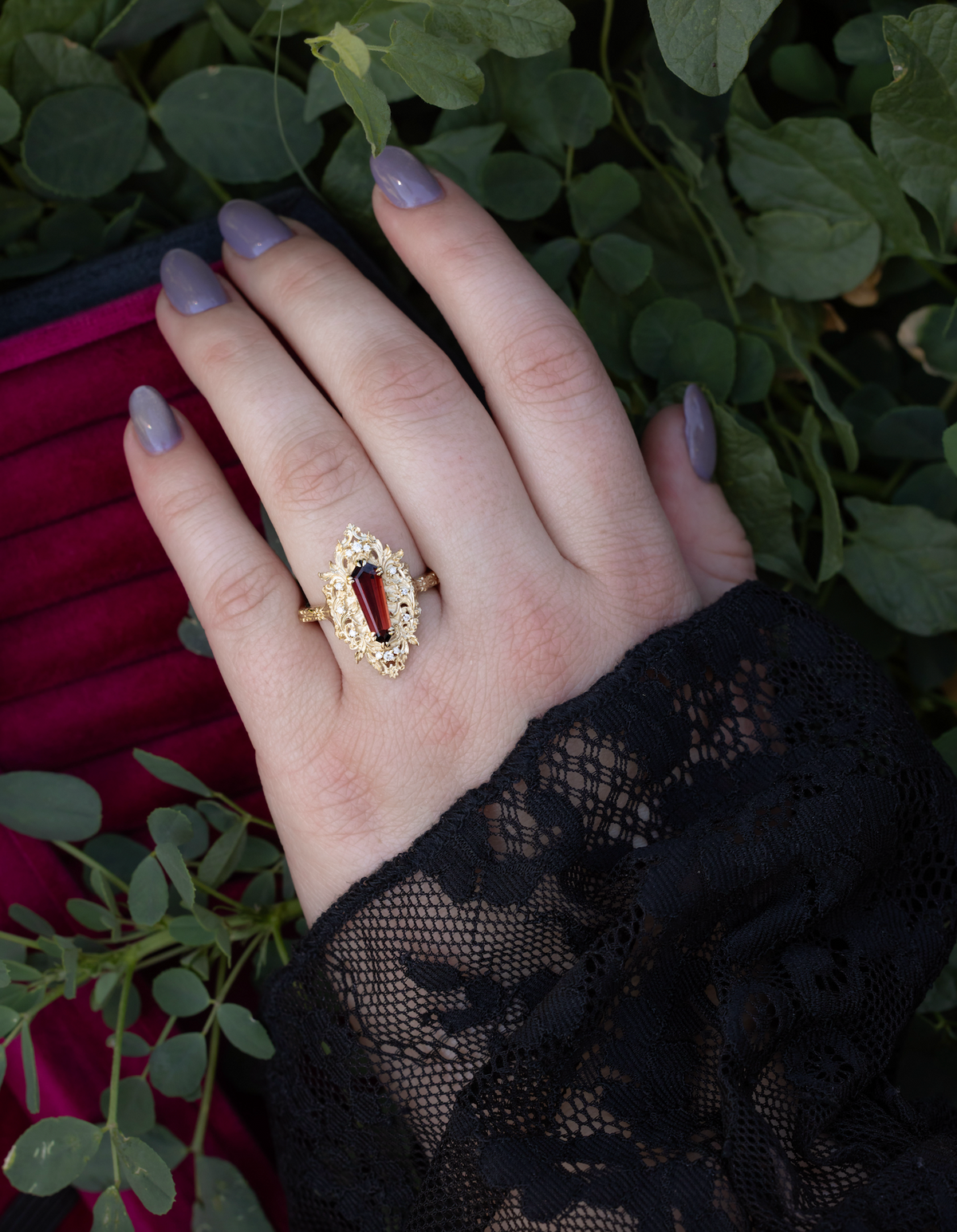 Hand wearing gold ring with garnet center stone against a foliage background