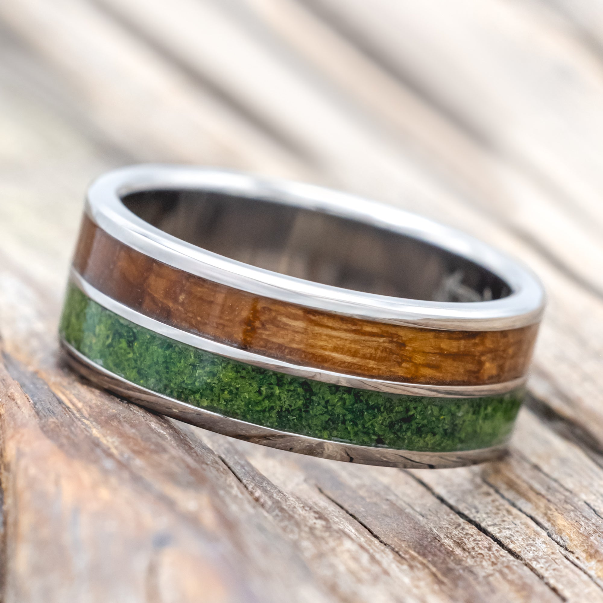 Titanium ring with whiskey barrel and moss inlay on a wooden surface