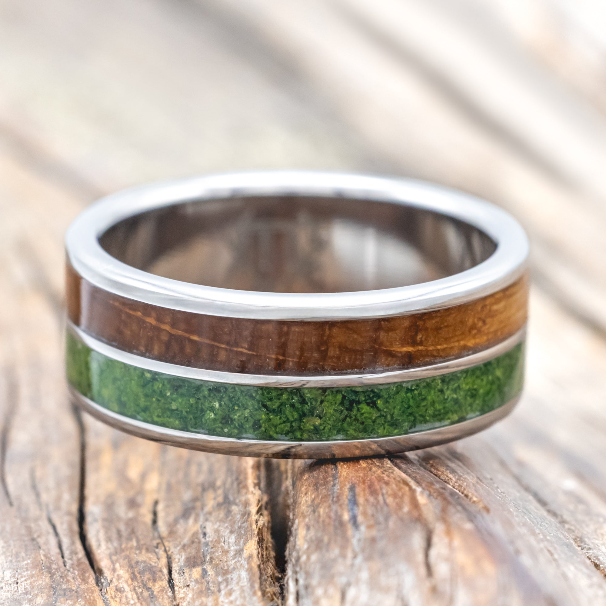 Titanium ring with whiskey barrel and moss inlay on a wooden surface
