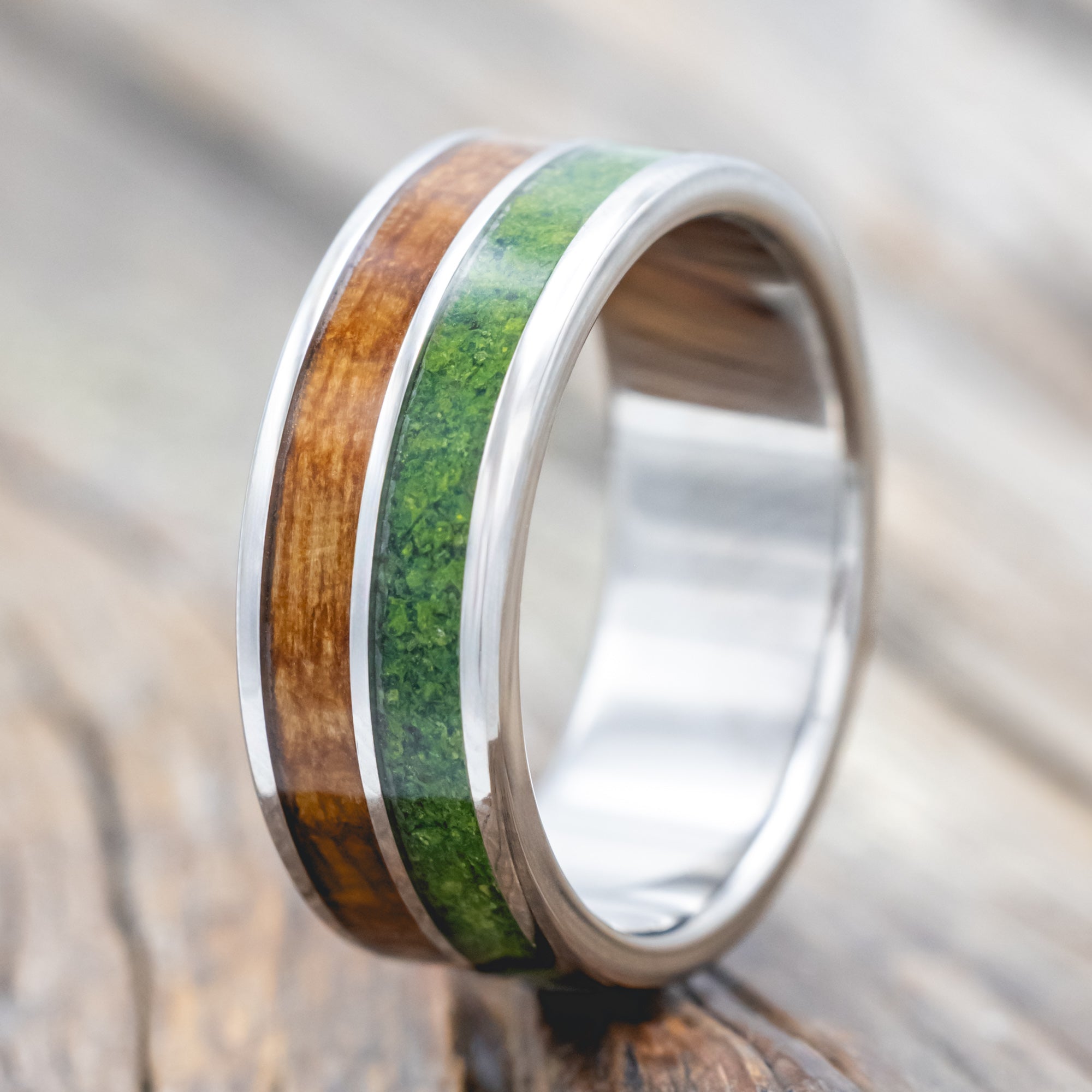Titanium ring with whiskey barrel and moss inlay on a wooden surface