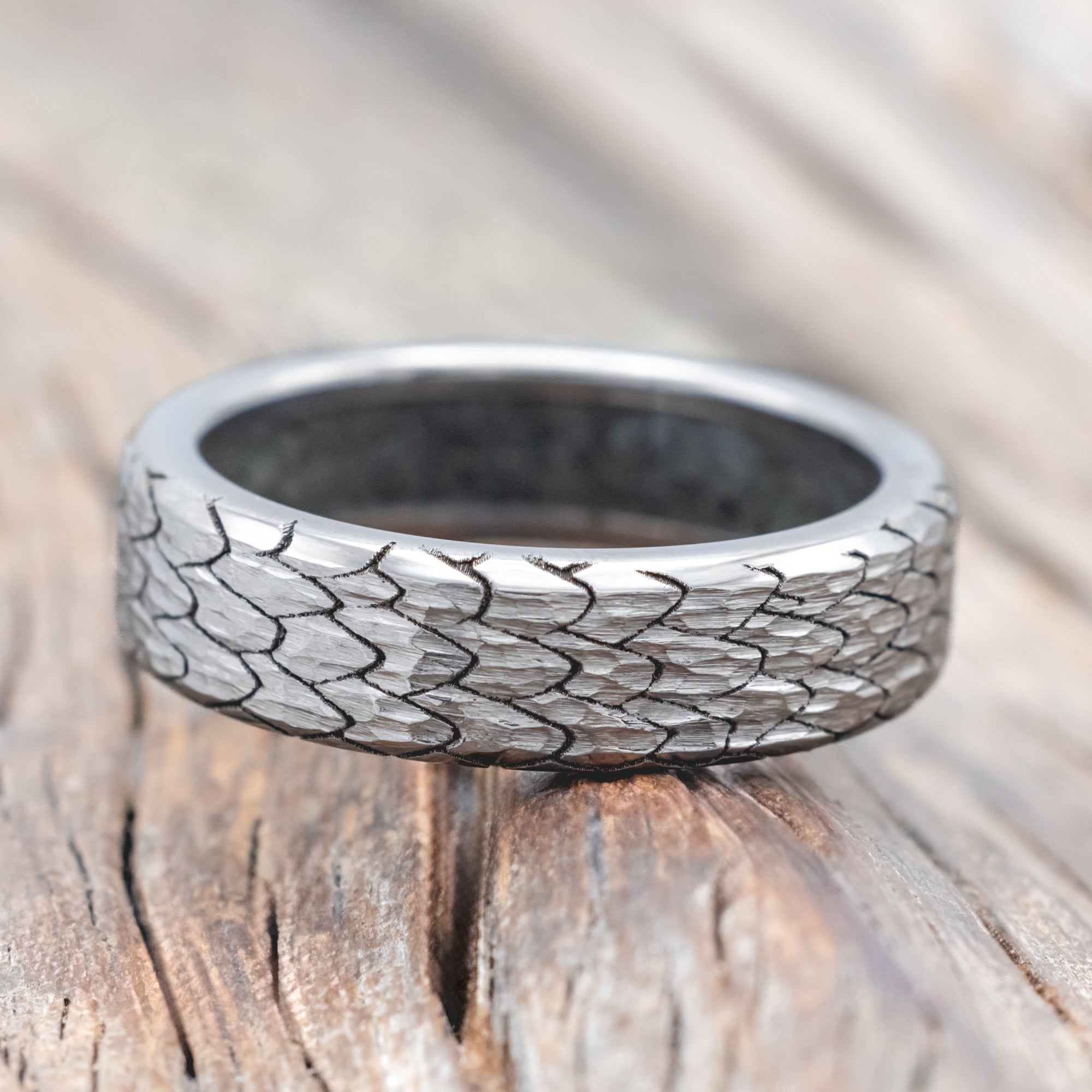 Titanium ring with textured dragon scale design on a wooden surface