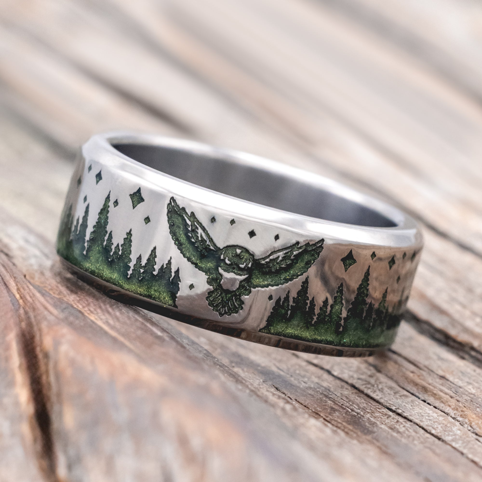 Titanium ring with owl, star and tree engraving with mystic moss inlay on a wooden surface