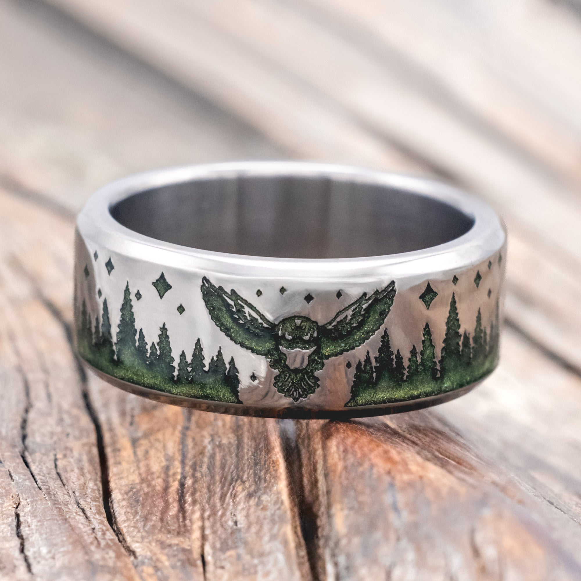 Titanium ring with owl, star and tree engraving with mystic moss inlay on a wooden surface