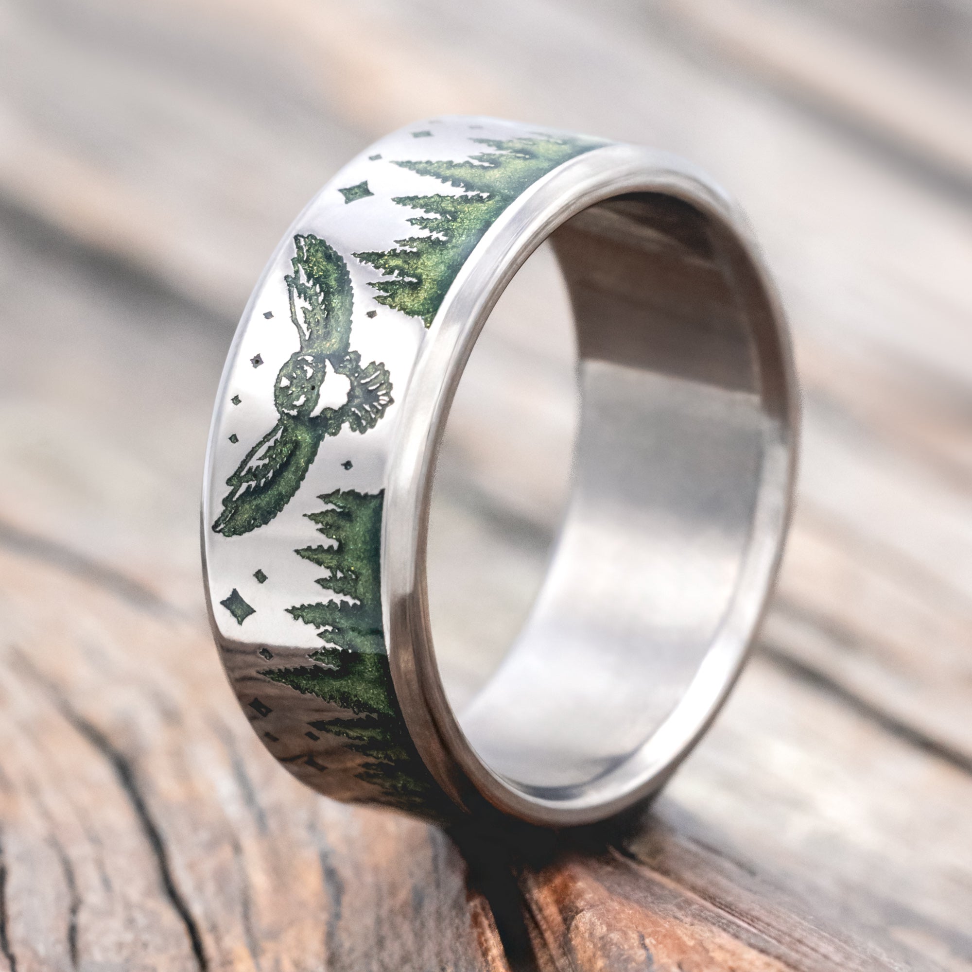 Titanium ring with owl, star and tree engraving with mystic moss inlay on a wooden surface