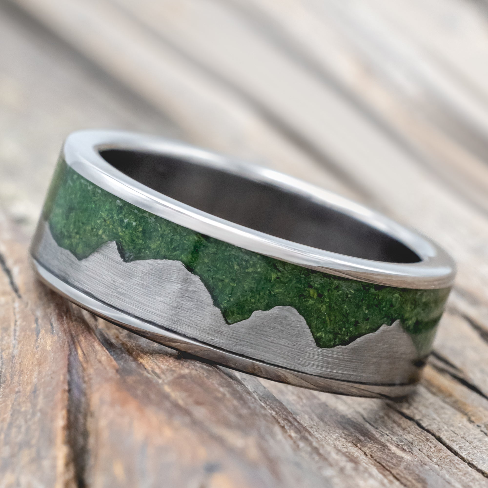 Titanium ring with moss inlay and titanium mountains on a wooden surface