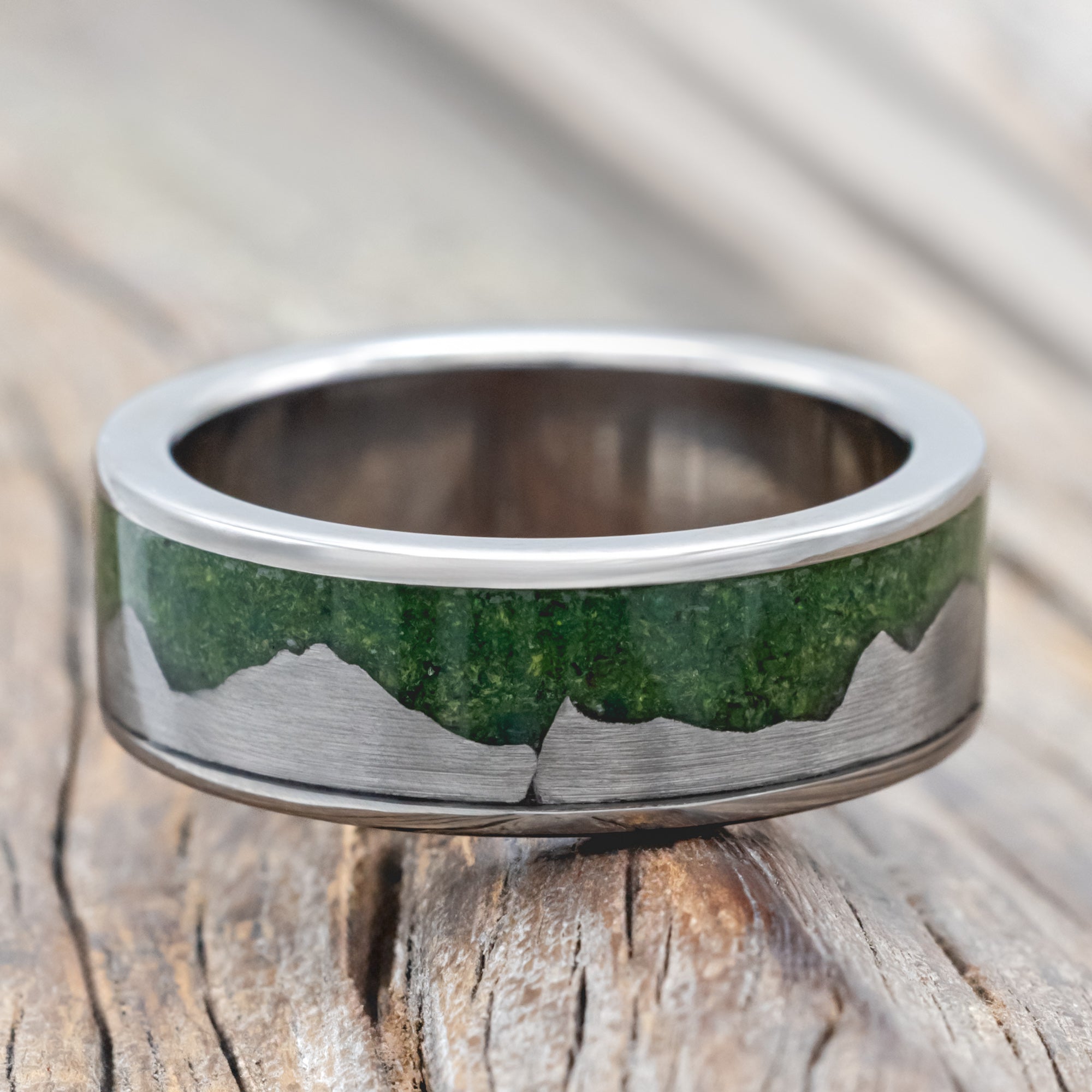 Titanium ring with moss inlay and titanium mountains on a wooden surface