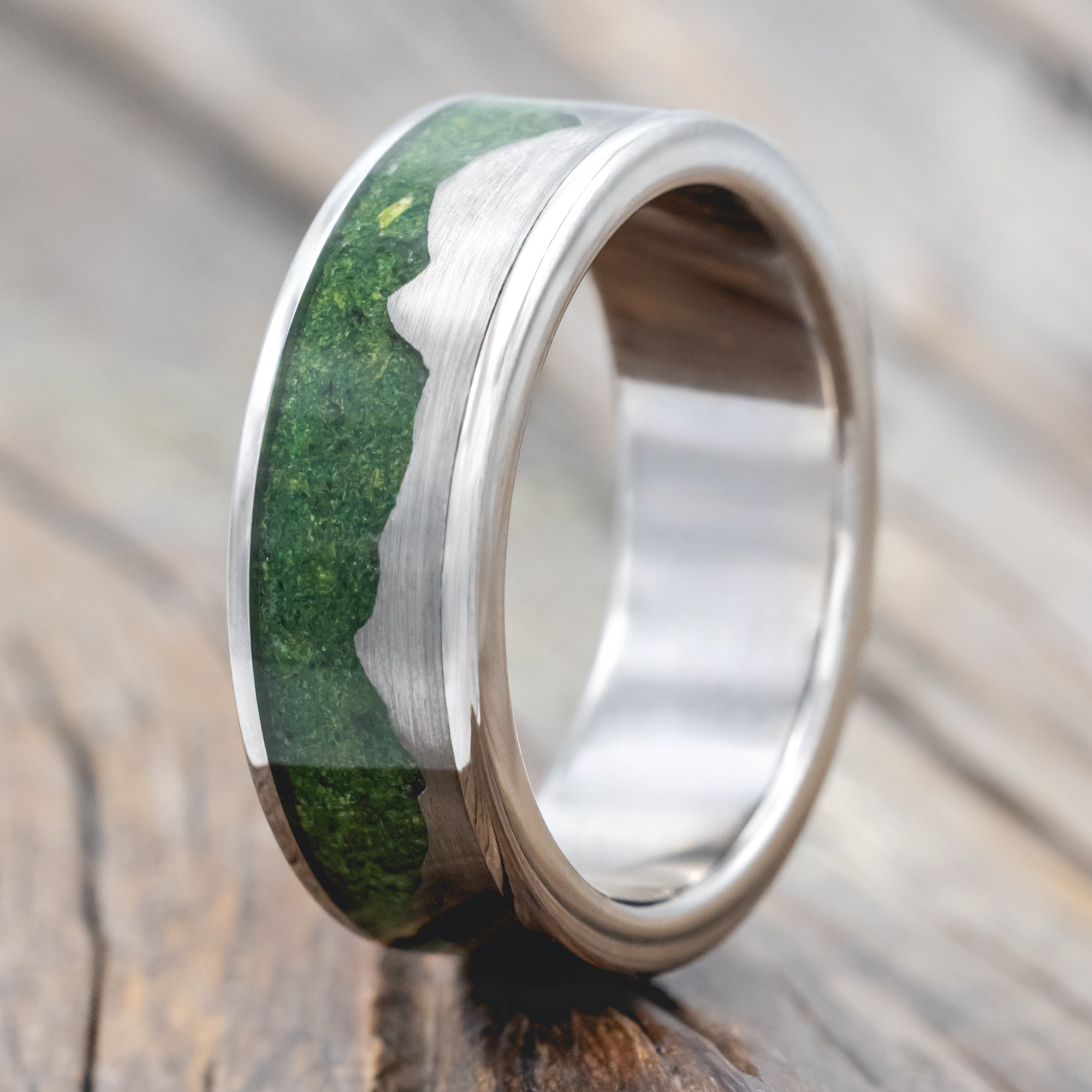 Titanium ring with moss inlay and titanium mountains on a wooden surface