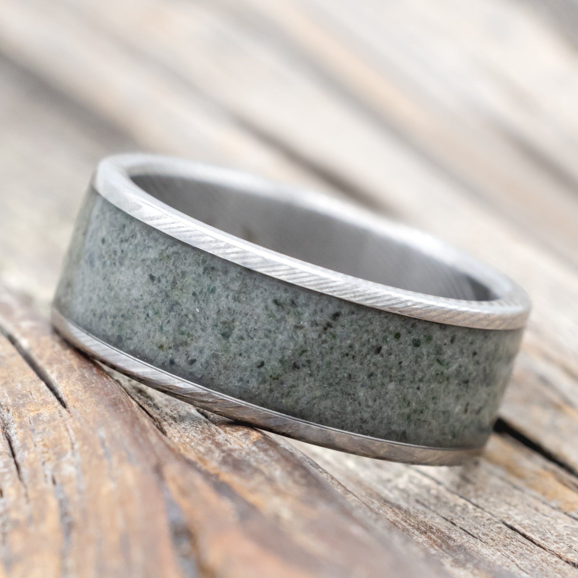 A Damascus steel ring with crushed moss agate inlay against a wooden background