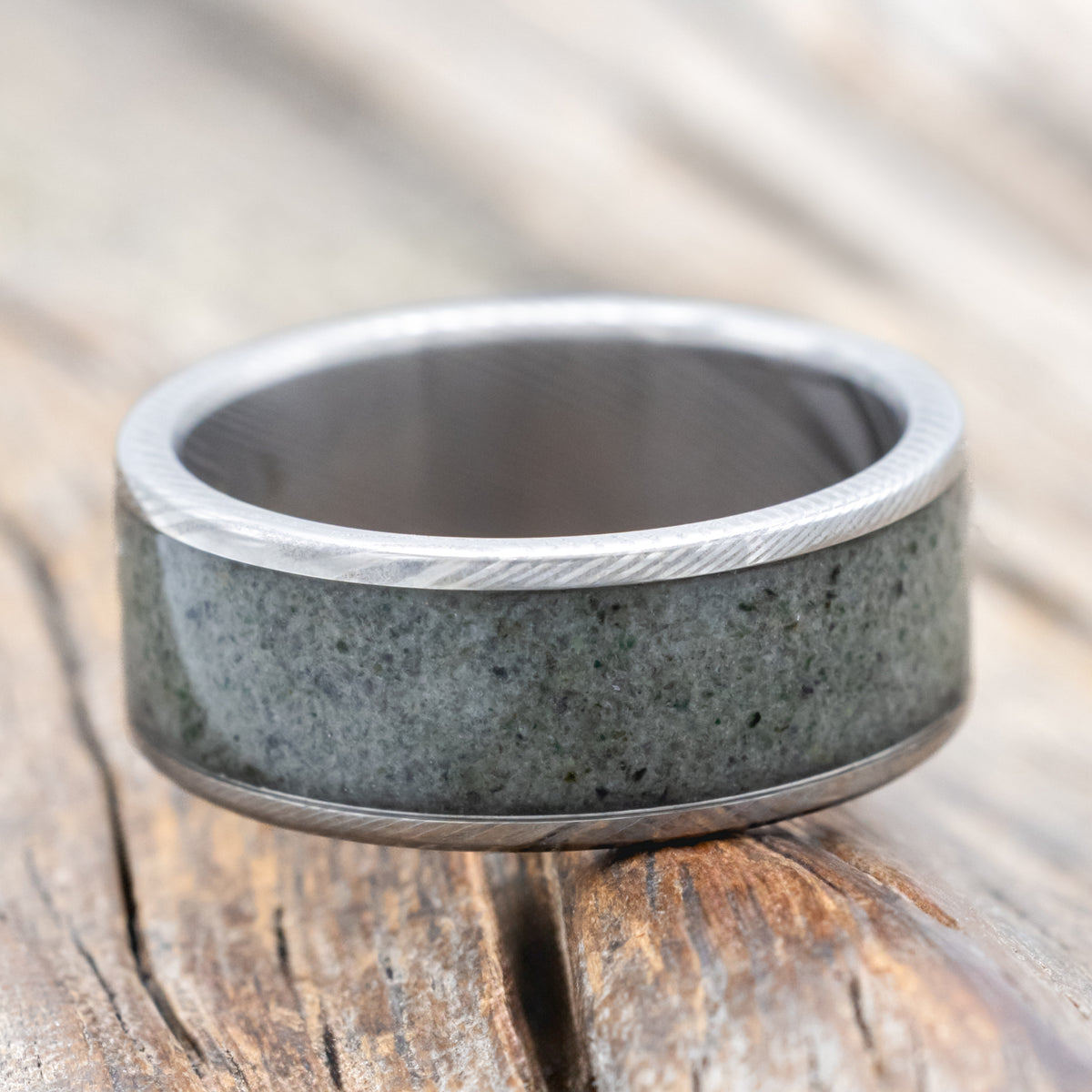 A Damascus steel ring with crushed moss agate inlay against a wooden background