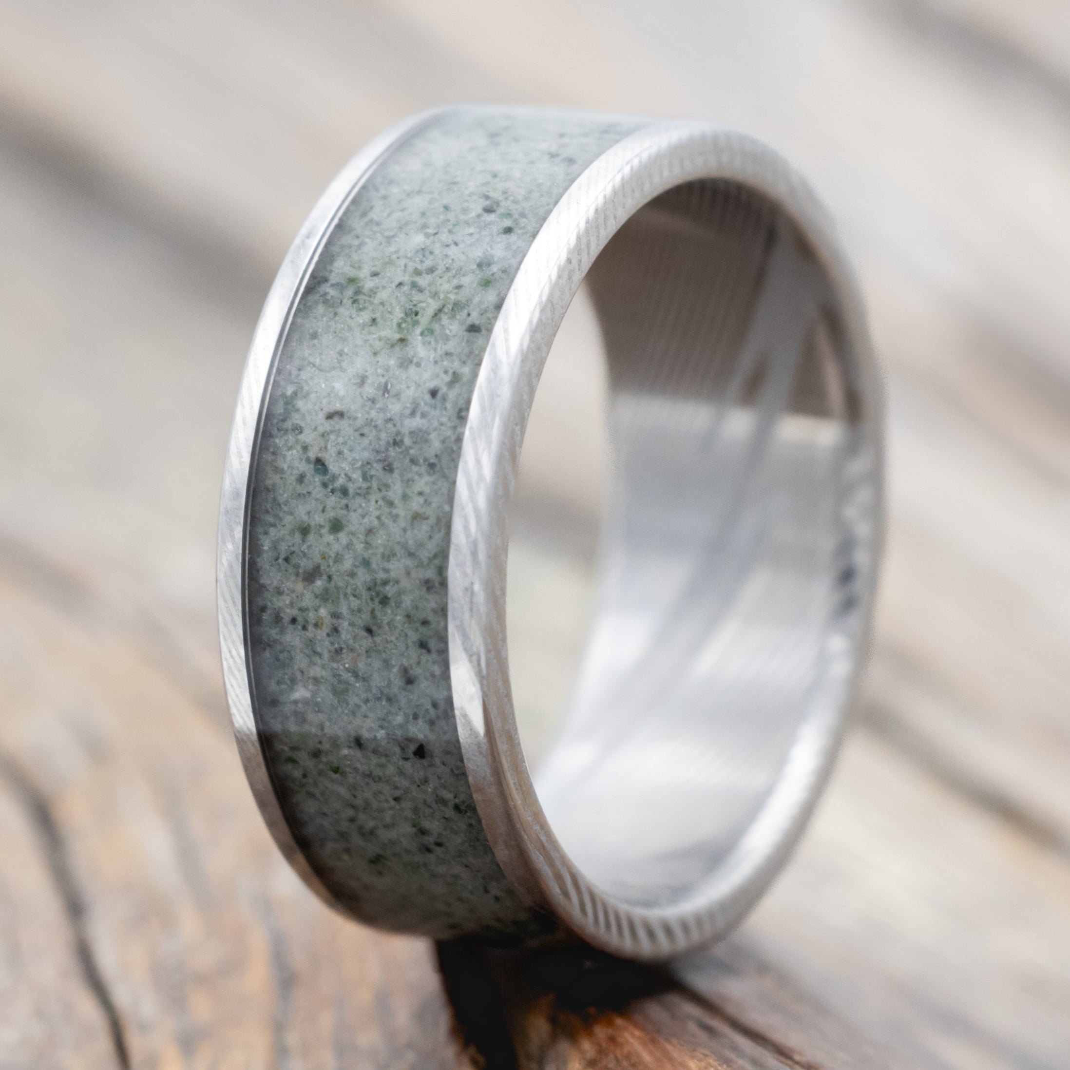 A Damascus steel ring with crushed moss agate inlay against a wooden background