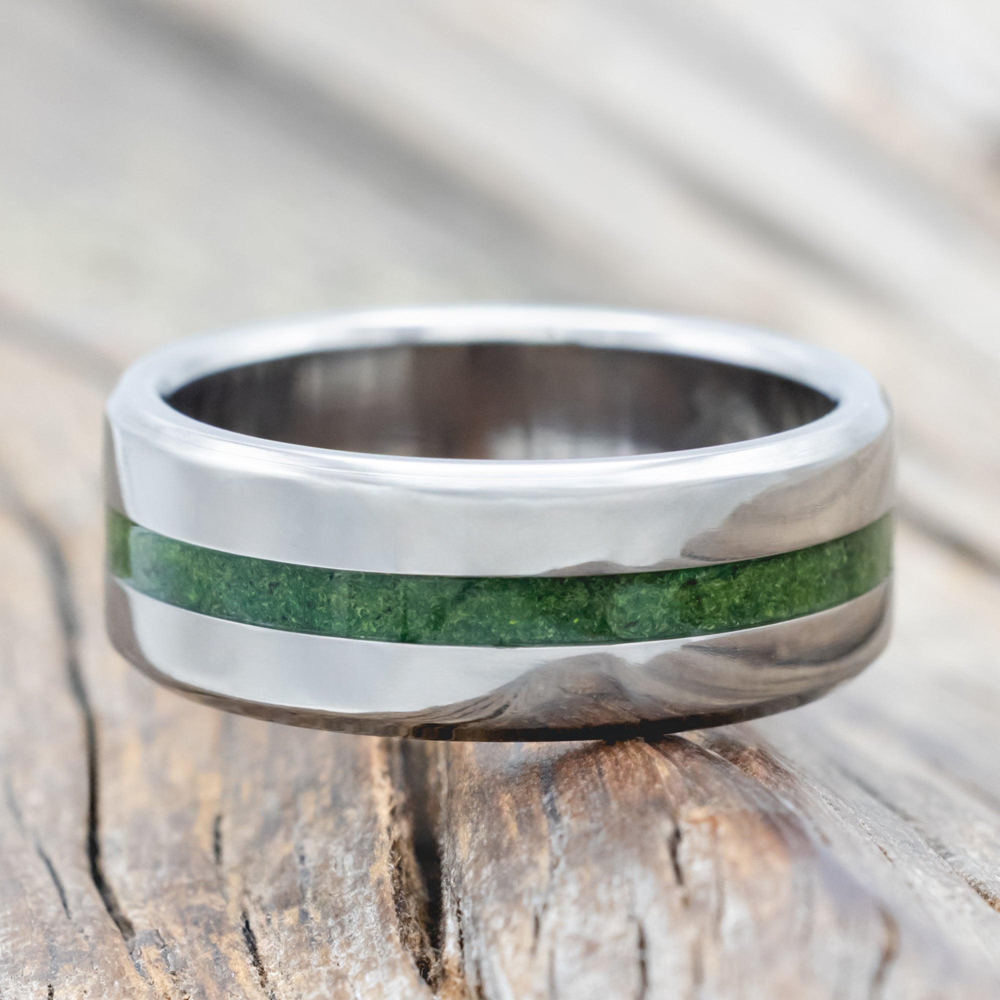 Titanium ring with moss inlay on a wooden surface
