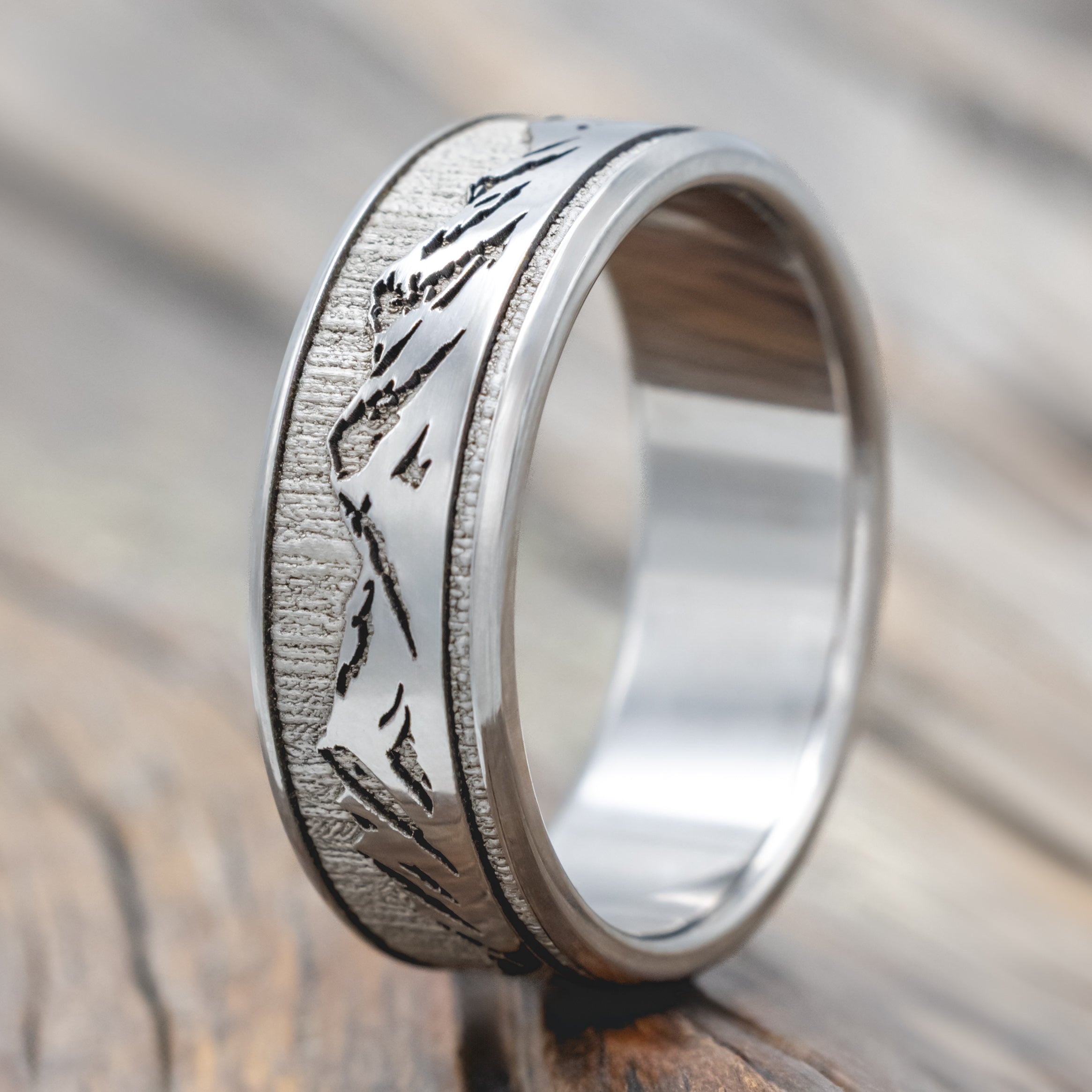 A titanium mountain ring with an engraved landscape design, resting on a rustic wooden surface.