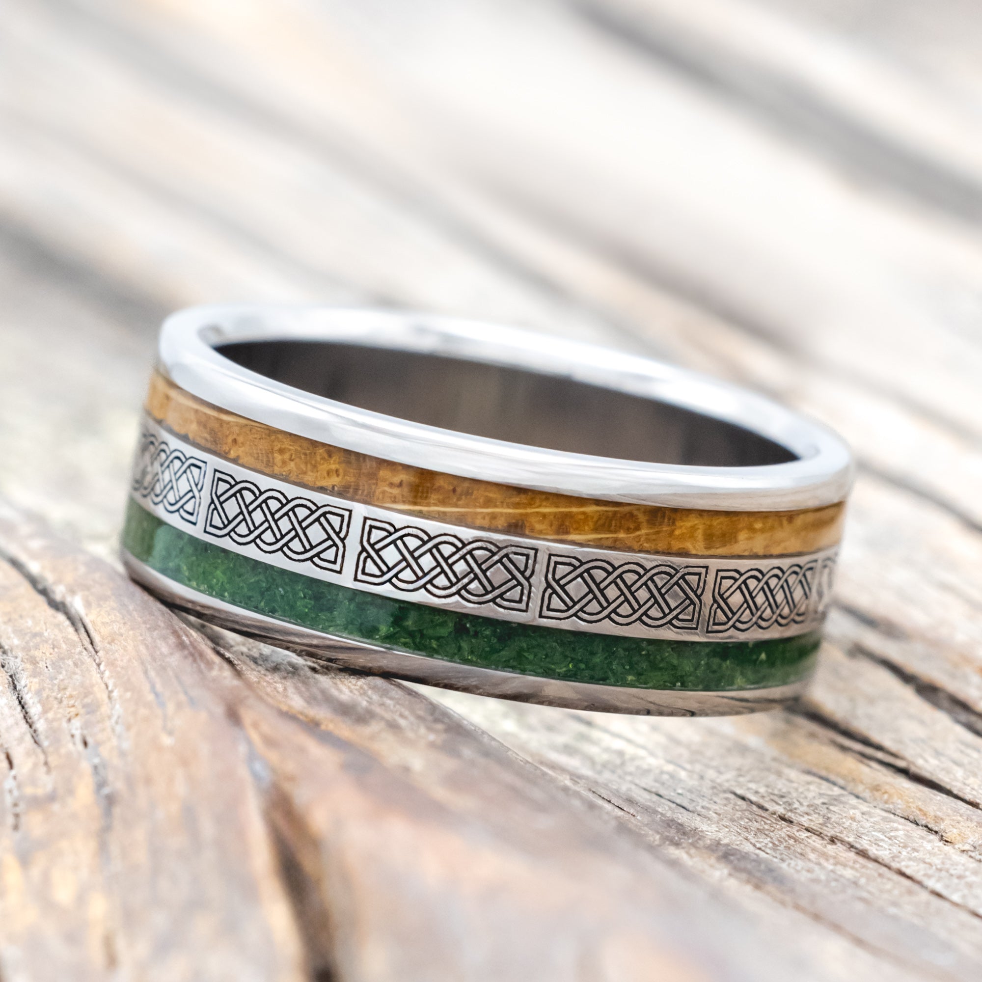 Titanium ring with moss and whiskey barrel oak inlays & Celtic knot engraving on wooden surface