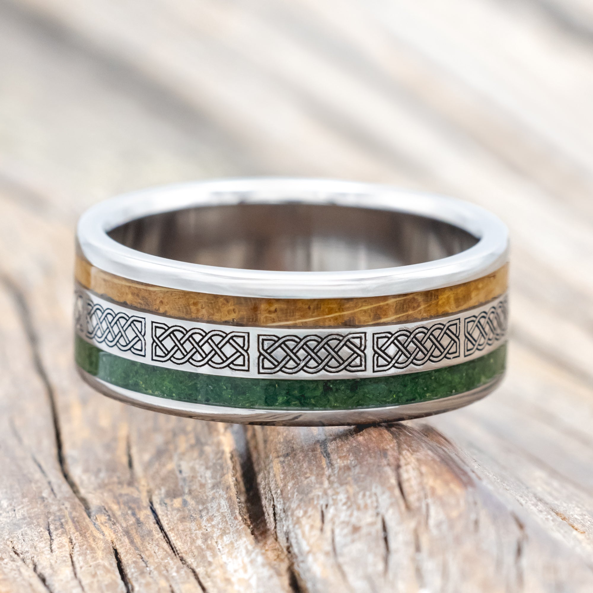 Titanium ring with moss and whiskey barrel oak inlays & Celtic knot engraving on wooden surface