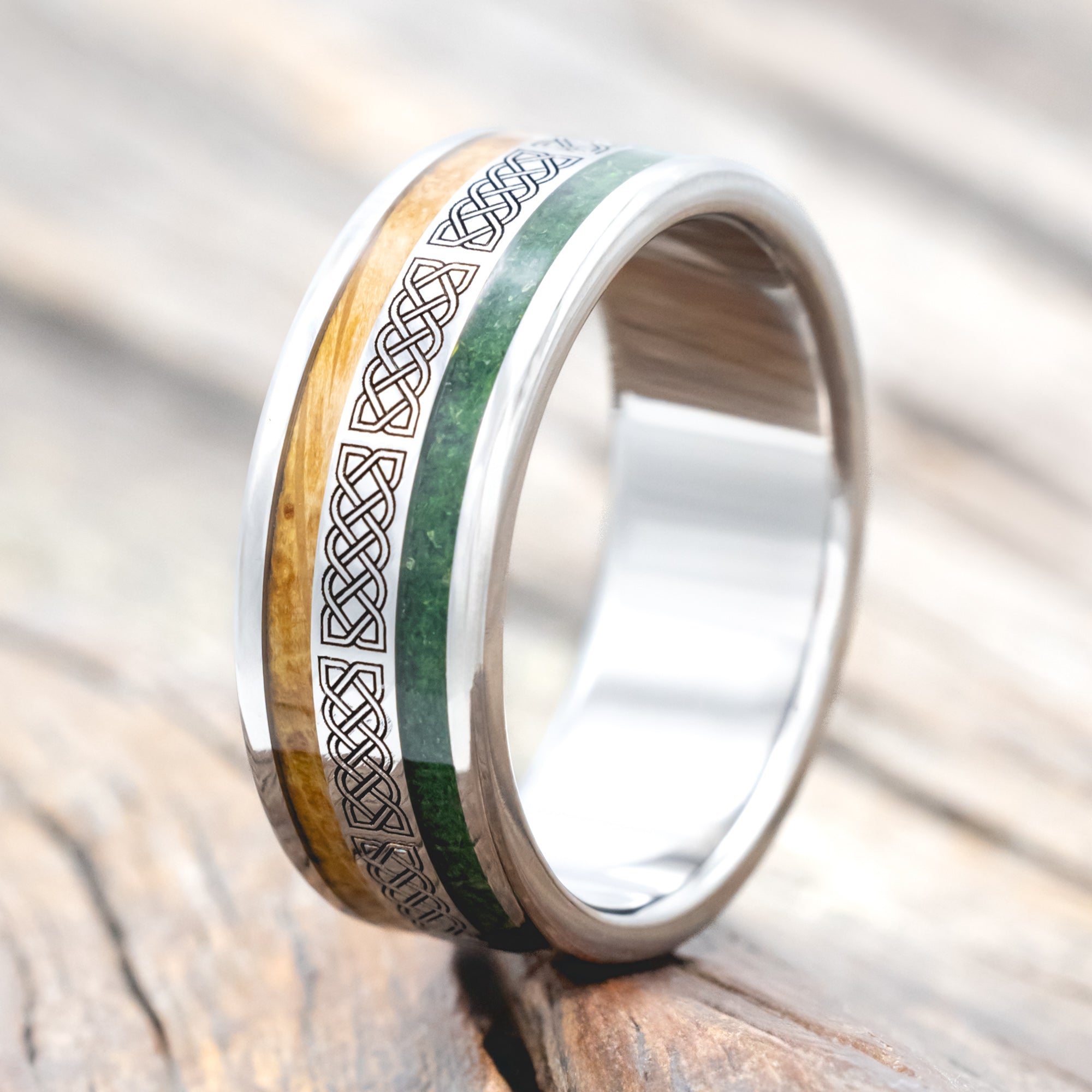 Titanium ring with moss and whiskey barrel oak inlays & Celtic knot engraving on wooden surface