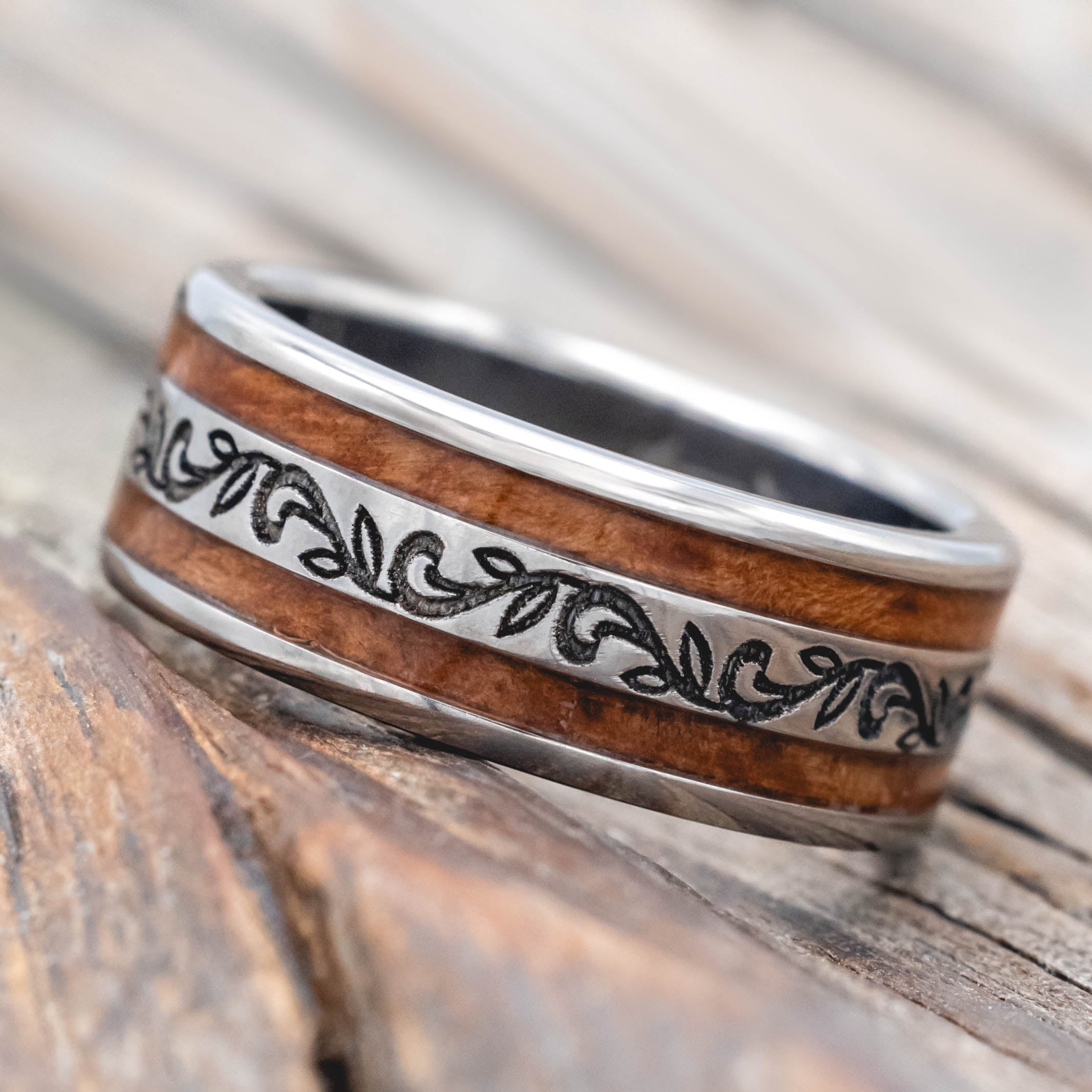 Silver ring with redwood inlay and paisley engraving on a wooden surface
