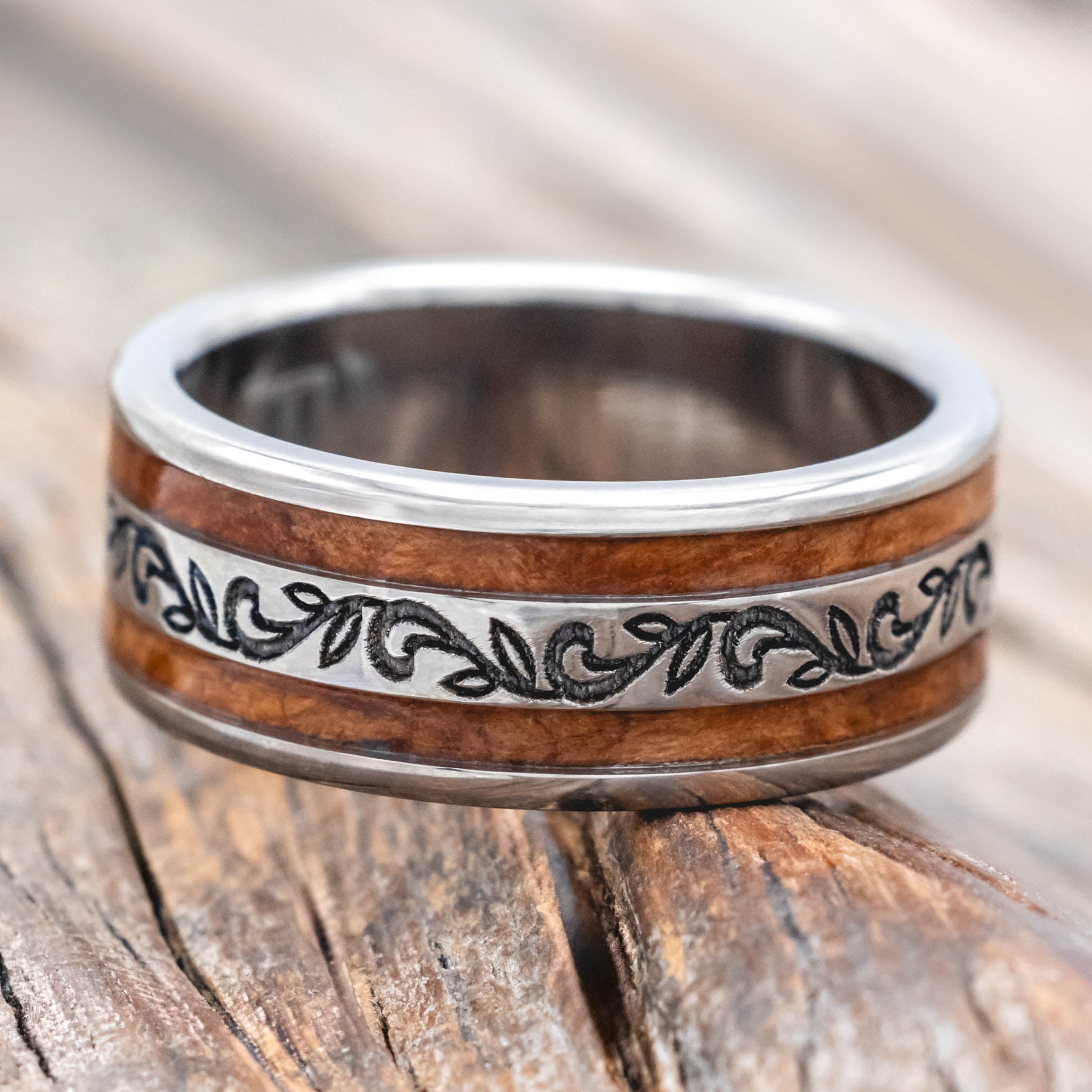 Silver ring with redwood inlay and paisley engraving on a wooden surface